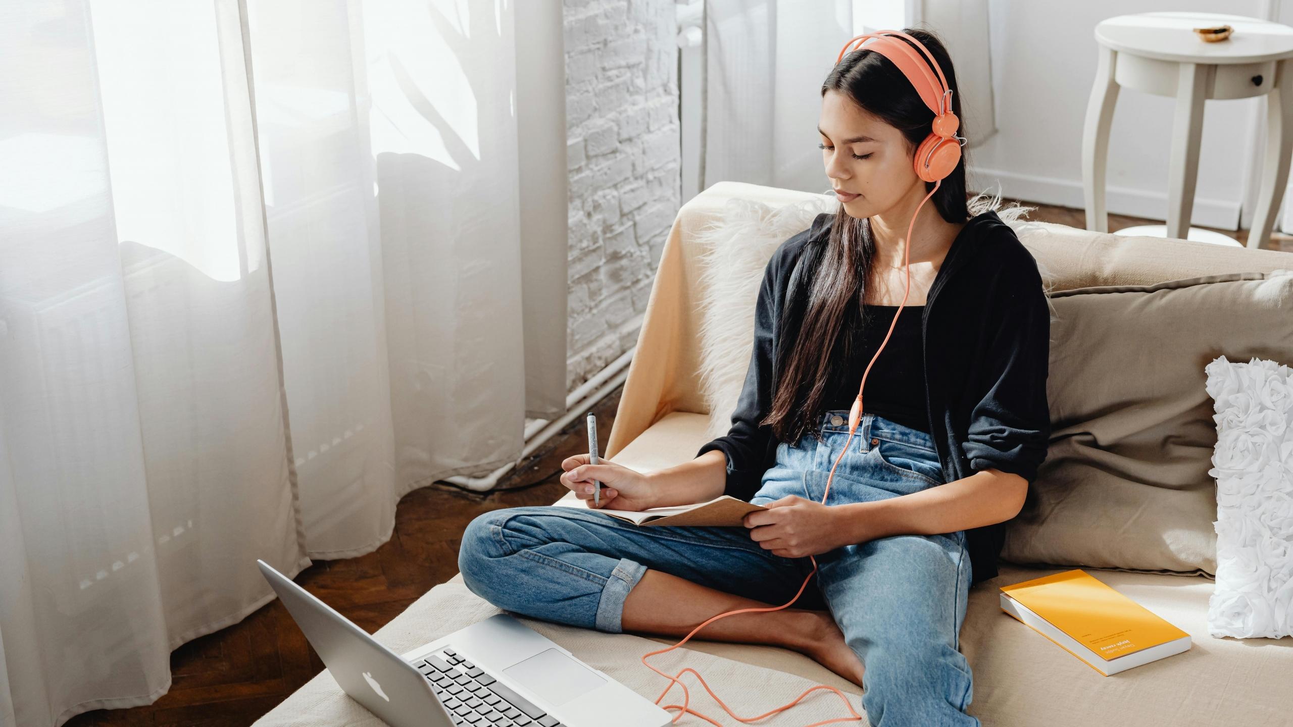 Imagen de una chica tomando nota mientras practica listening con audifonos 