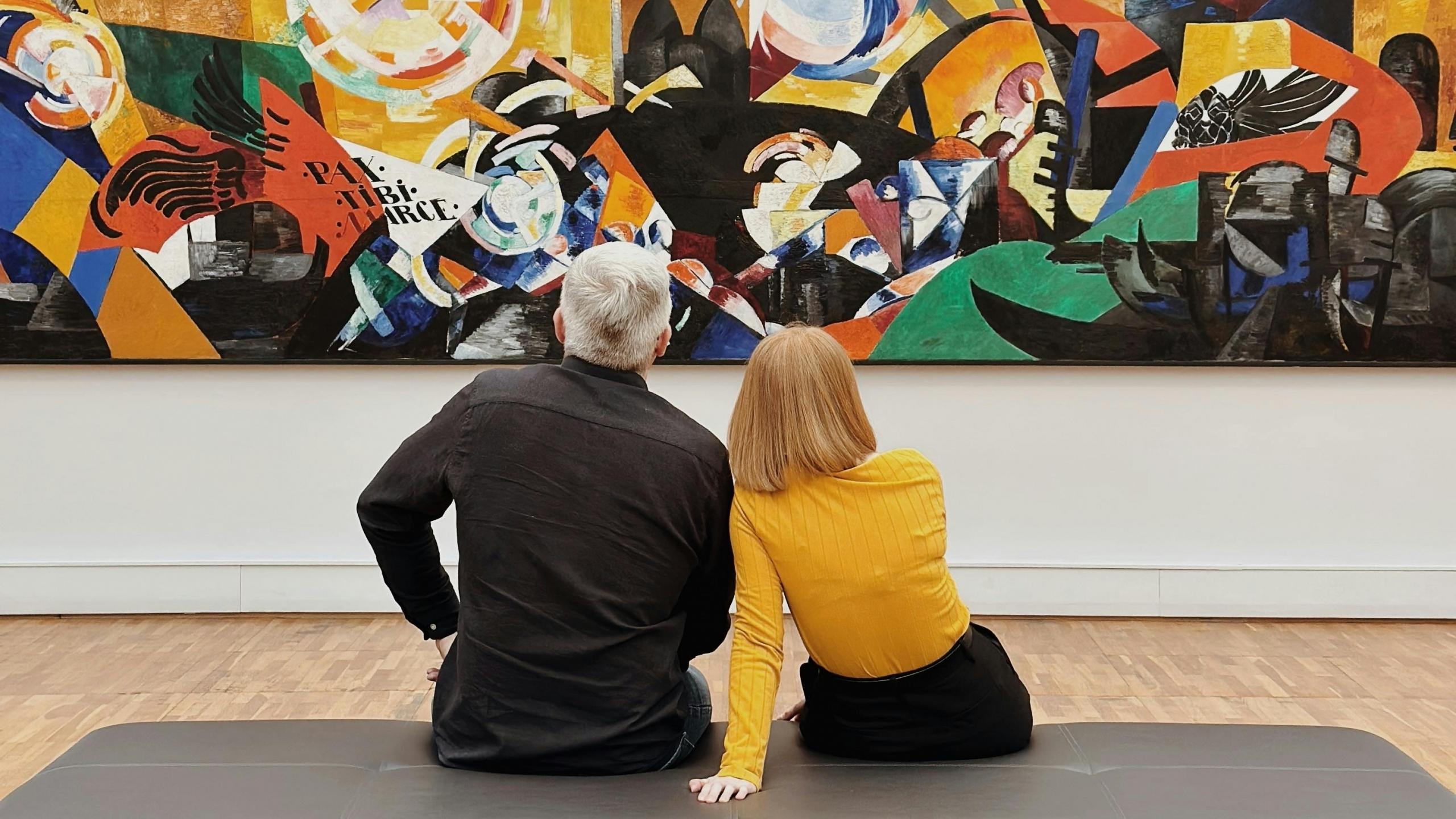 Imagen de dos personas observando una pintura geométrica en un museo