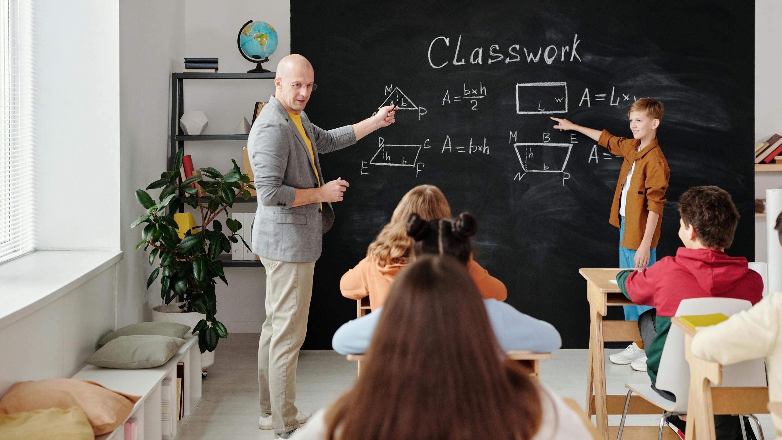 Imagen de estudiantes de primaria en un salón de clase con su profesor de matemáticas
