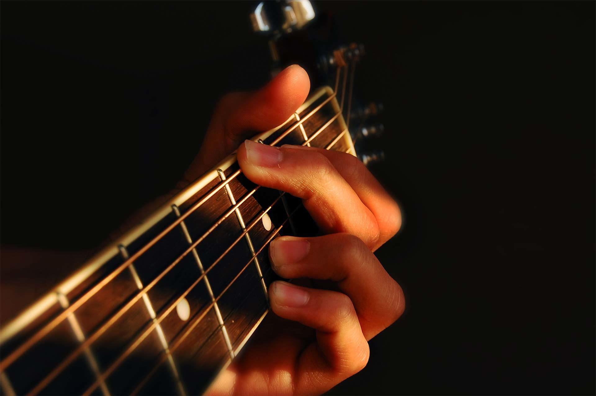 Manos puestas sobre los trastes de una guitarra.