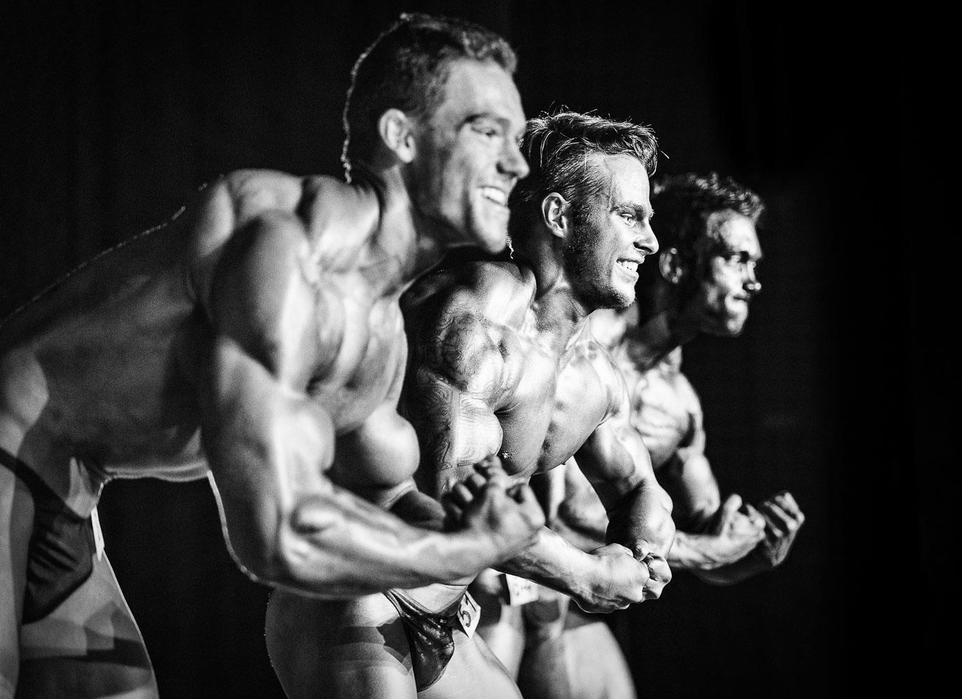 Tres hombres usando tanga masculina mostrando sus cuerpos tonificados y musculatura durante un concurso de Halterofilia.