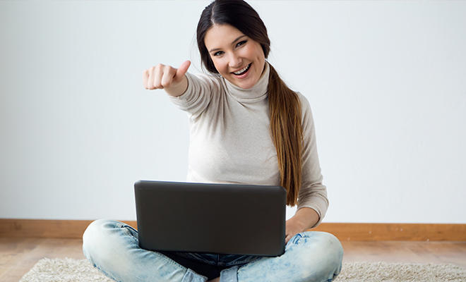Chica sentada con una laptop en sus piernas mientras sonríe y levanta la mano en señal de aprovacion.