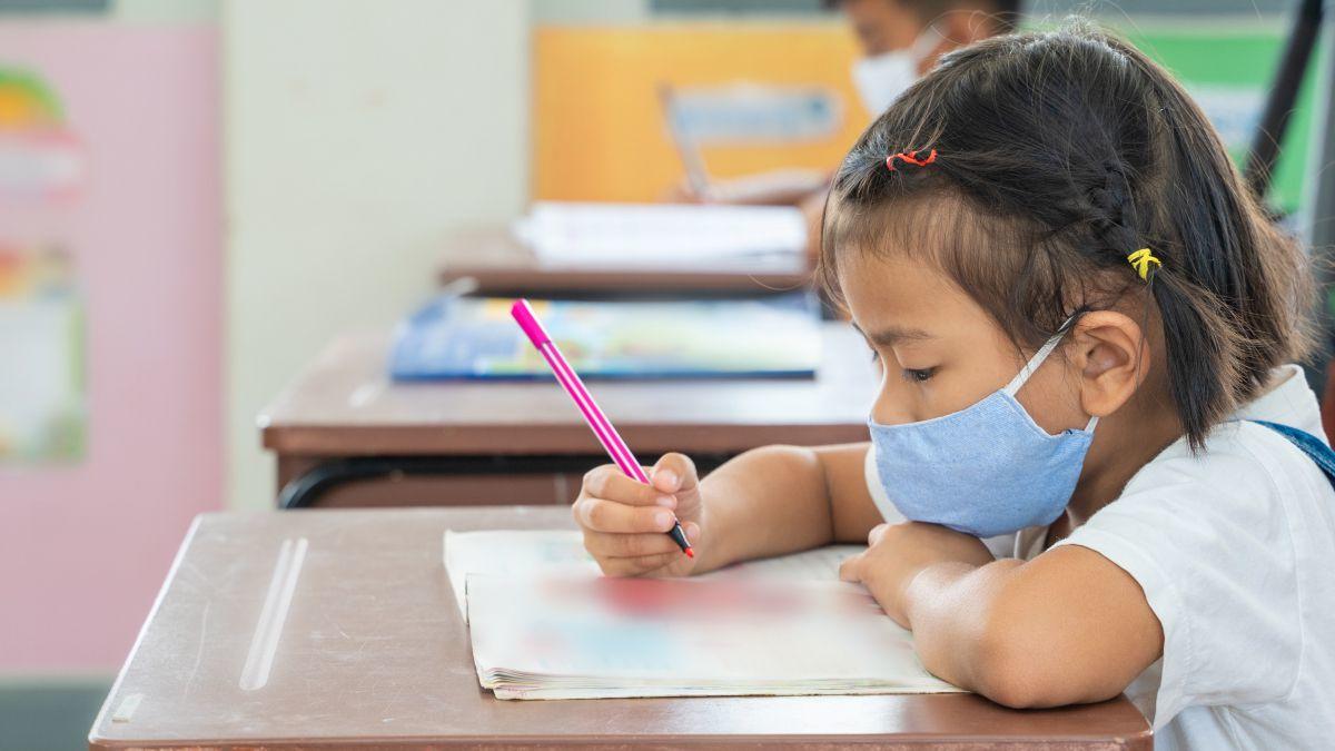Niña sentada en un pupitre, escribiendo en un cuaderno.