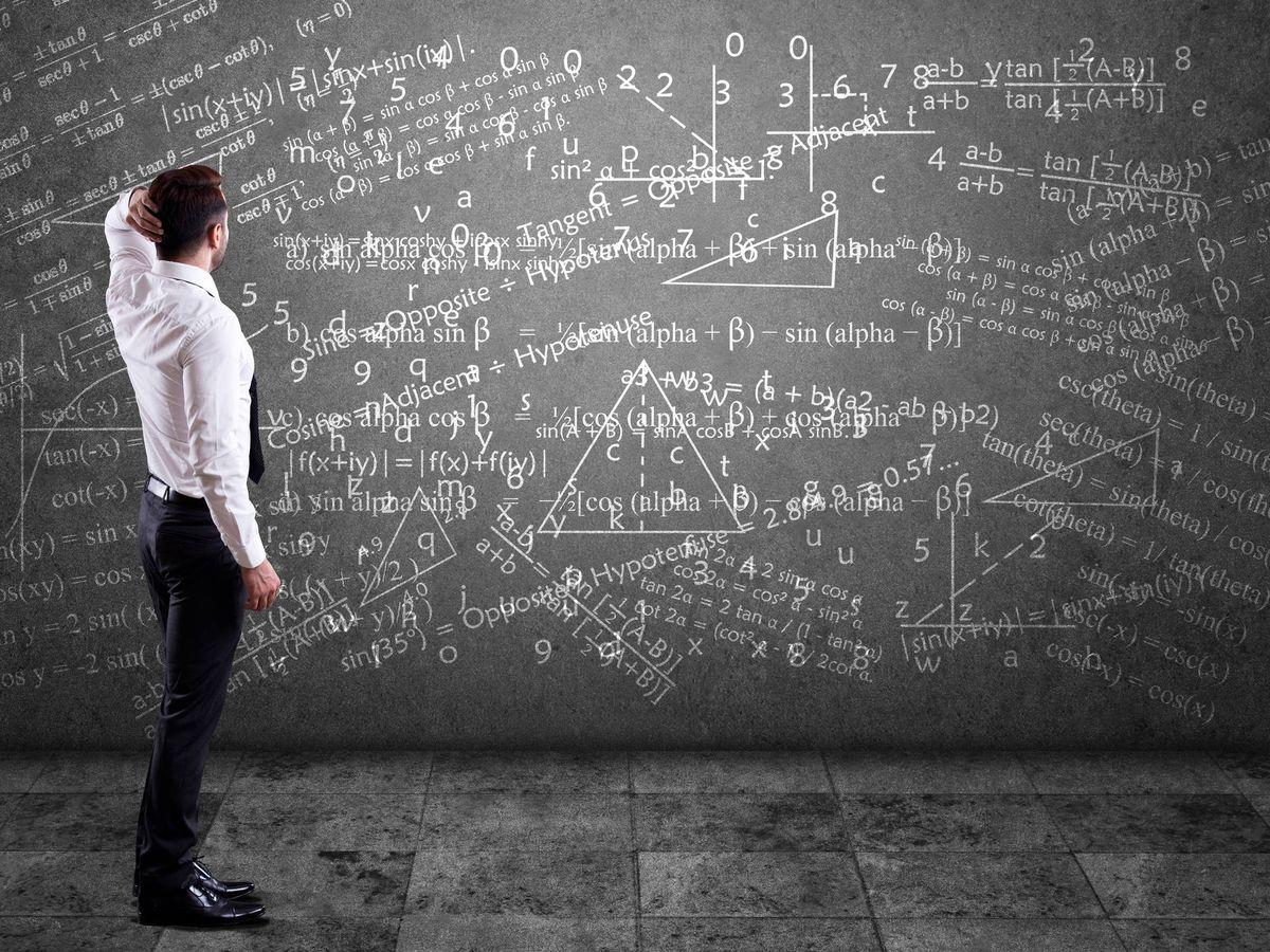 Hombre con su mano en la cabeza mientras observa un tablero con muchas ecuaciones matemáticas.