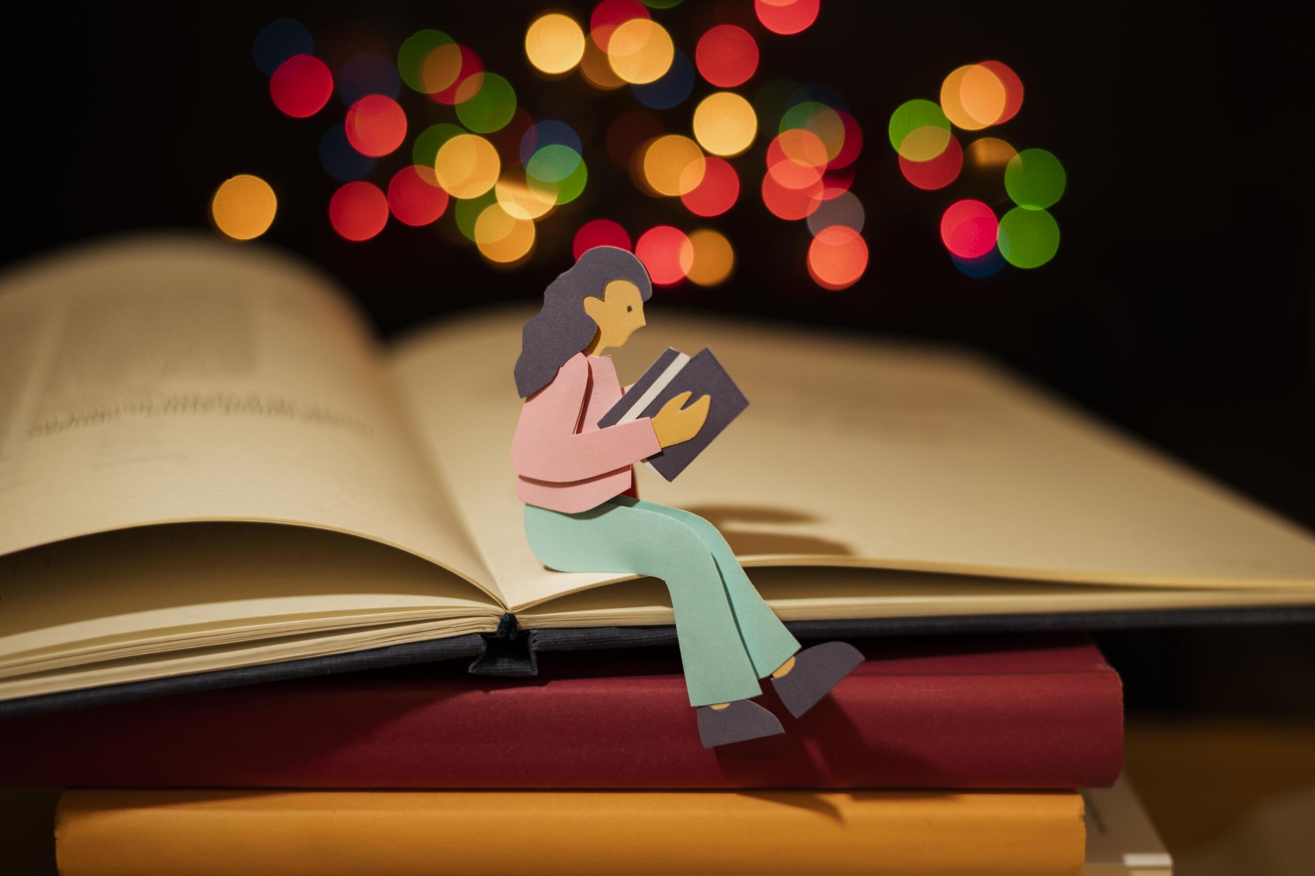 muñequito pequeño de papel con libro en mano sentado en las páginas de un libro abierto en tamaño real