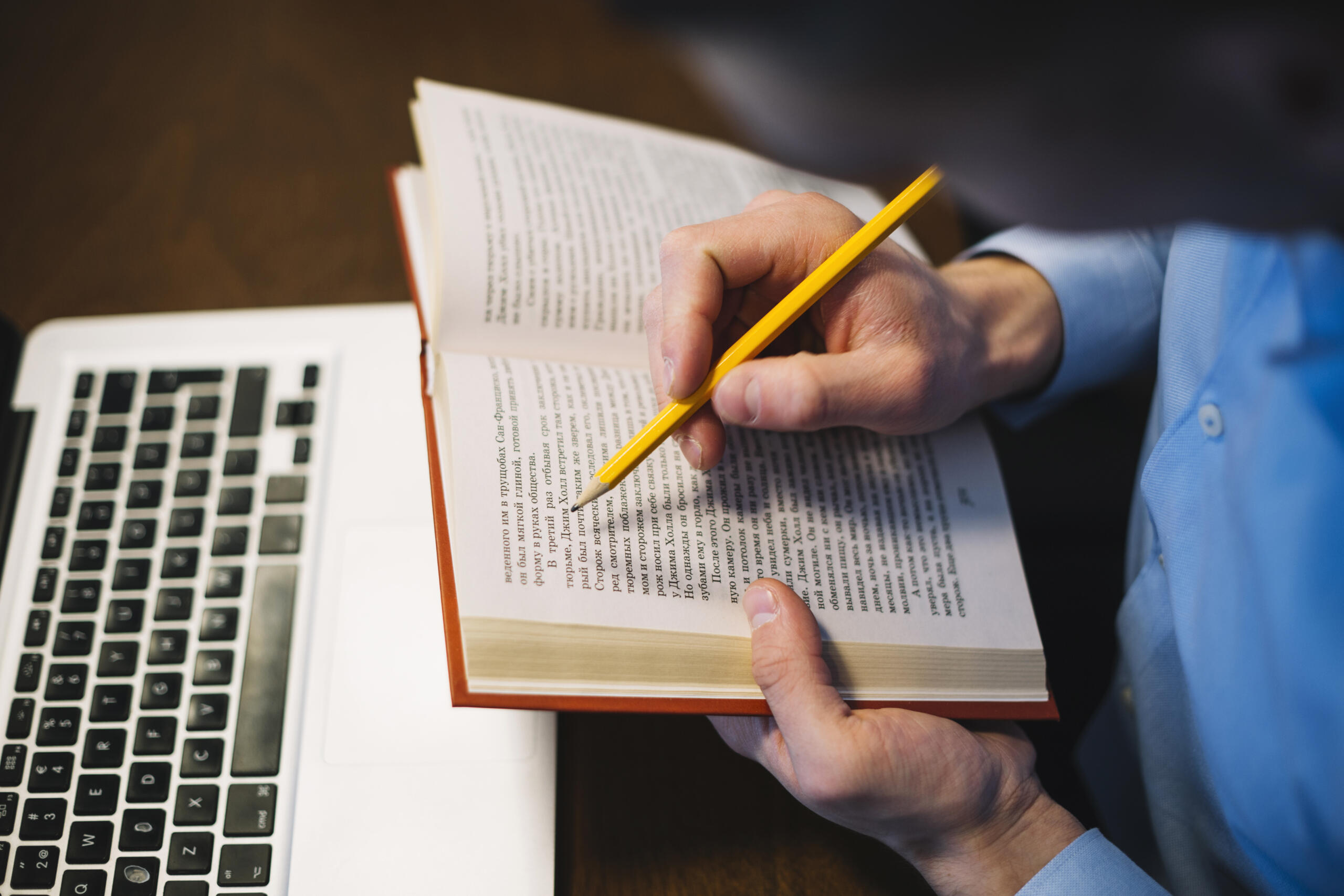 vista cenital de chico con un lápiz siguiendo lectura en su libro frente a la computadora