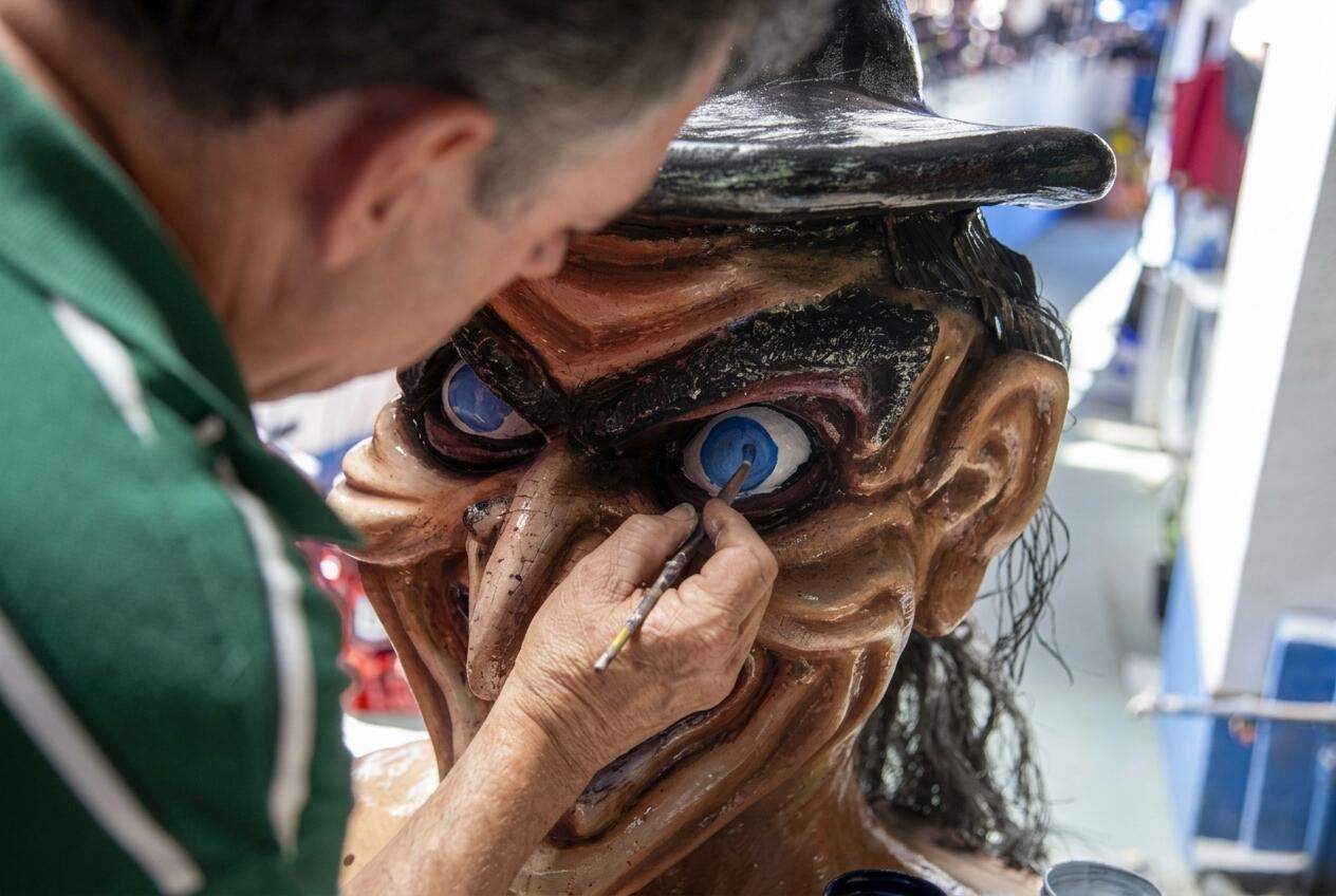 Un artista pinta el ojo azul de una gran escultura caricaturesca de una bruja que lleva un sombrero negro.