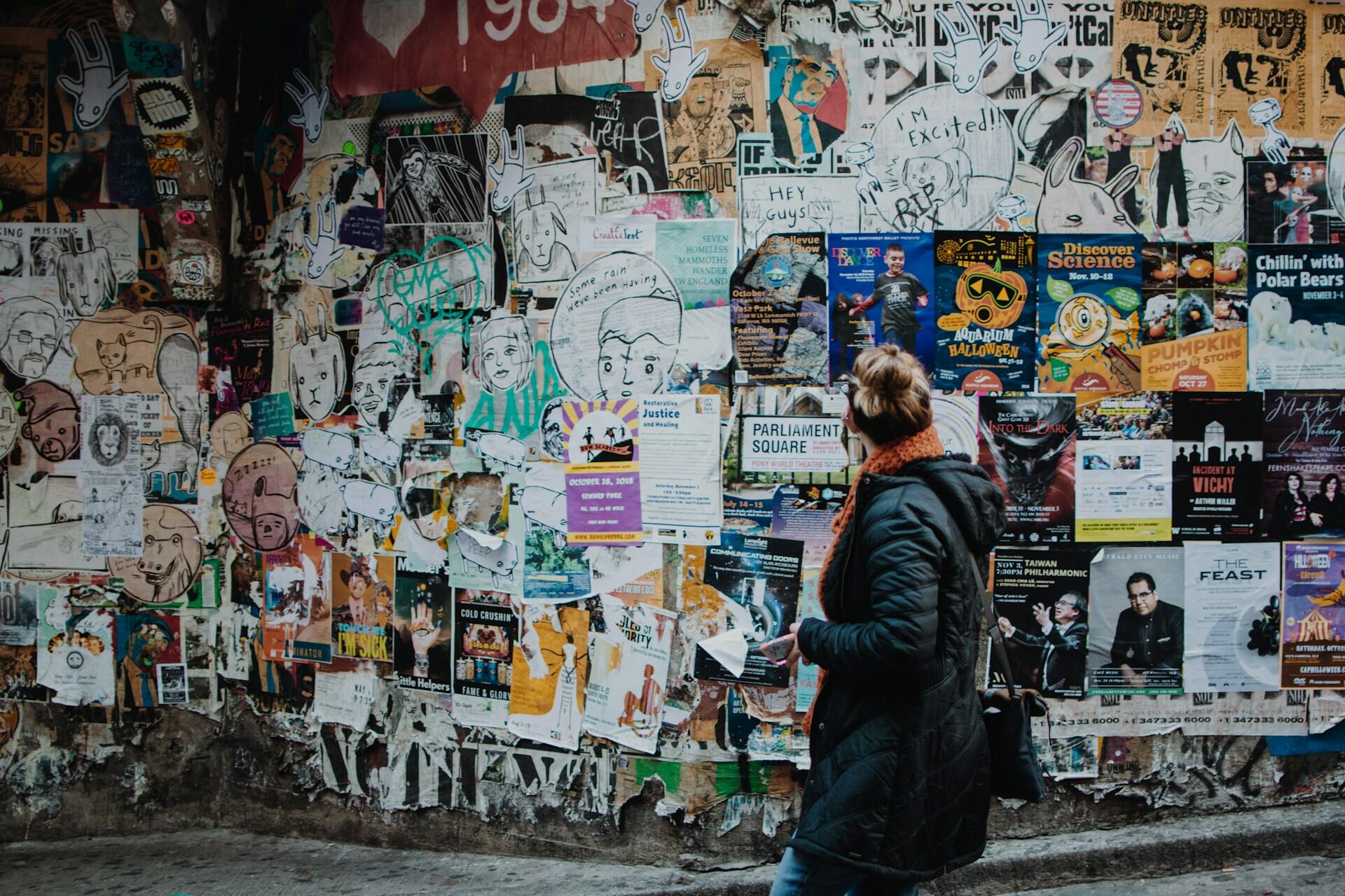 Frau läuft an vollgeklebter Wand vorbei.