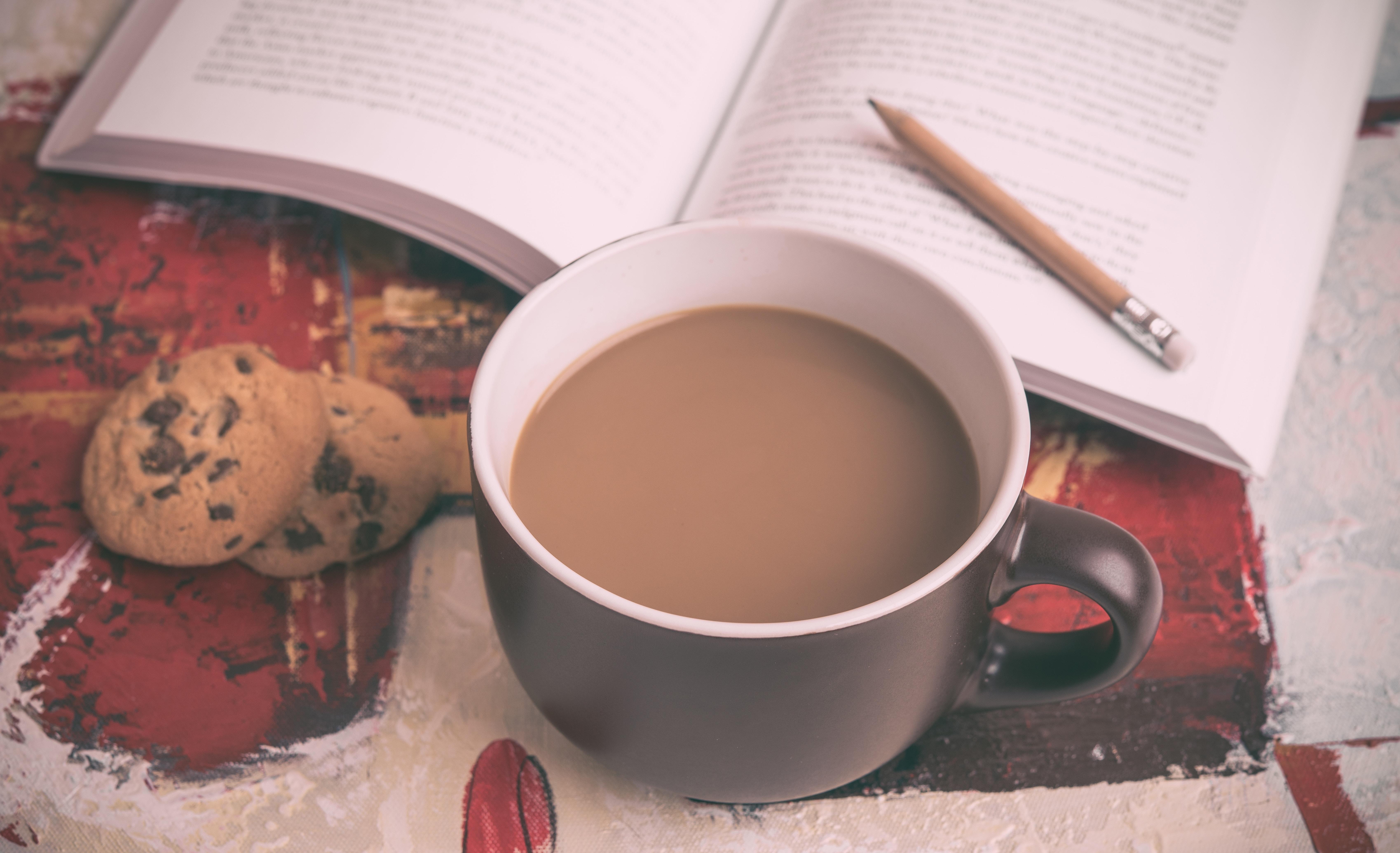 Tasse Kaffe neben aufgeschlagenem Buch und Keks.