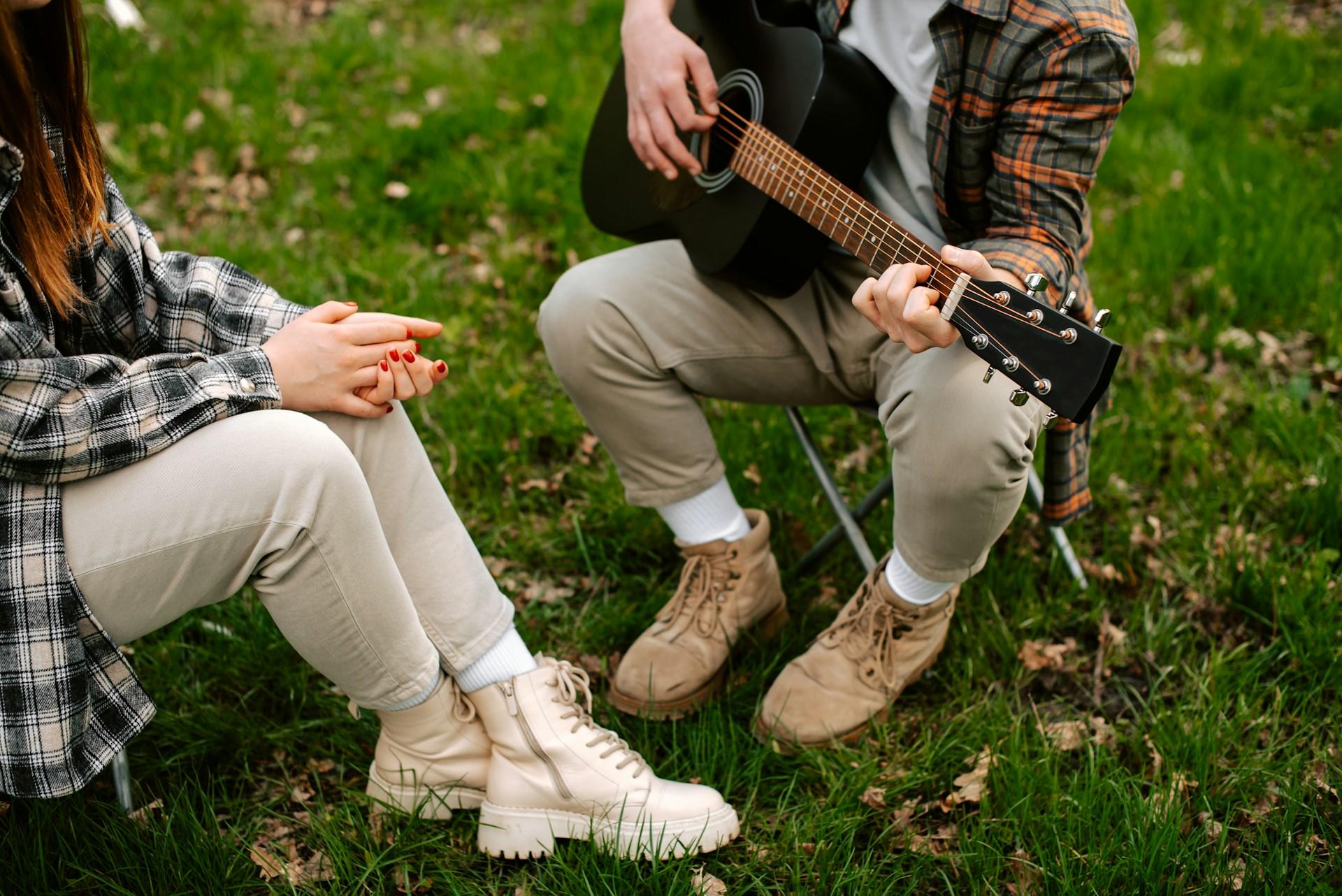Zwei Personen sitzen auf kleinen Stühlen auf dem Rasen und eine davon spielt Gitarre