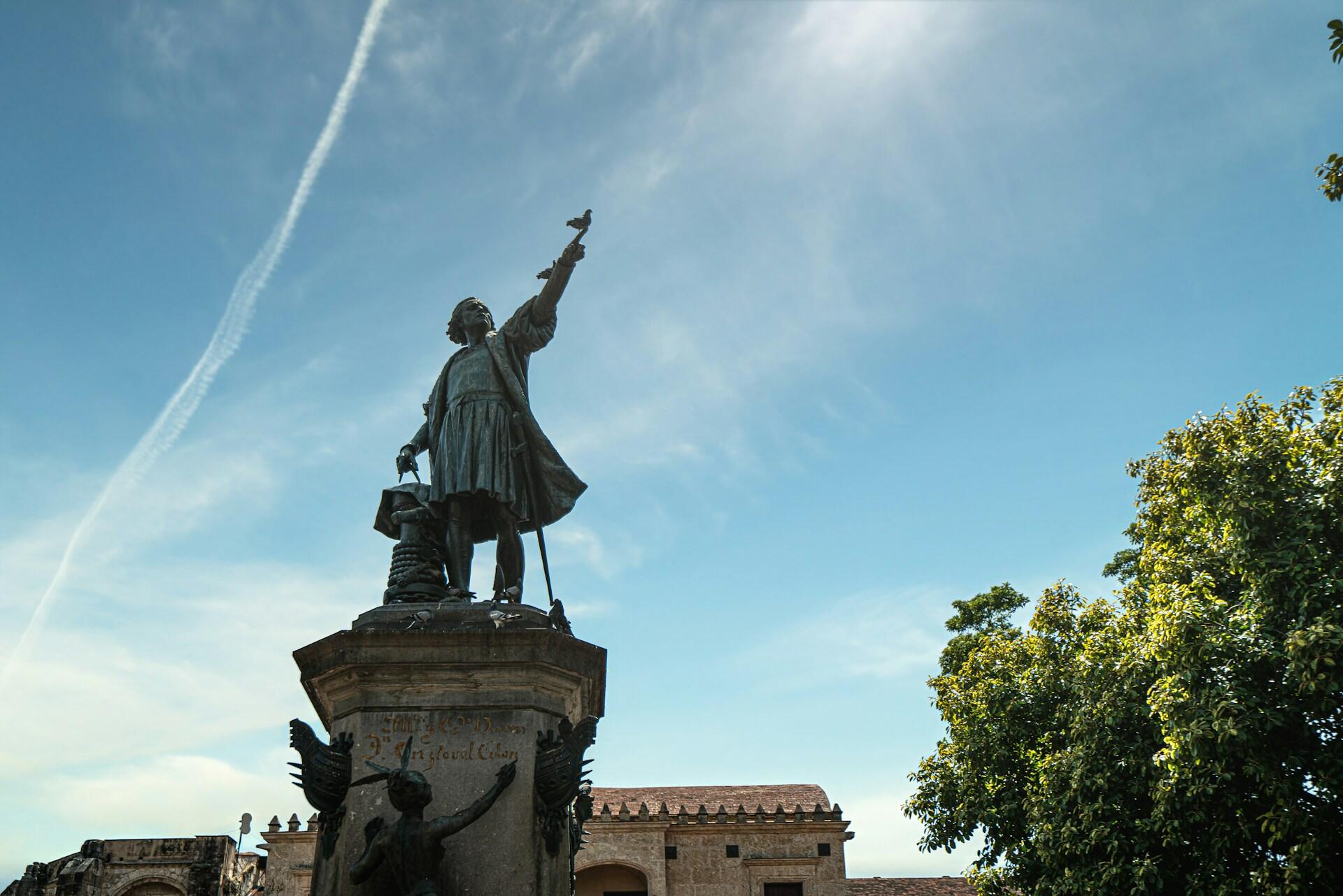 Statue von Mann mit ausgestrecktem Arm auf Sockel.