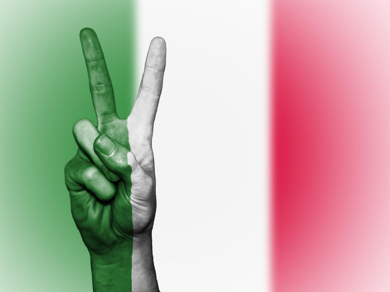 Grün-weiße Hand, die vor der italienischen Flagge das Peace-Zeichen macht.