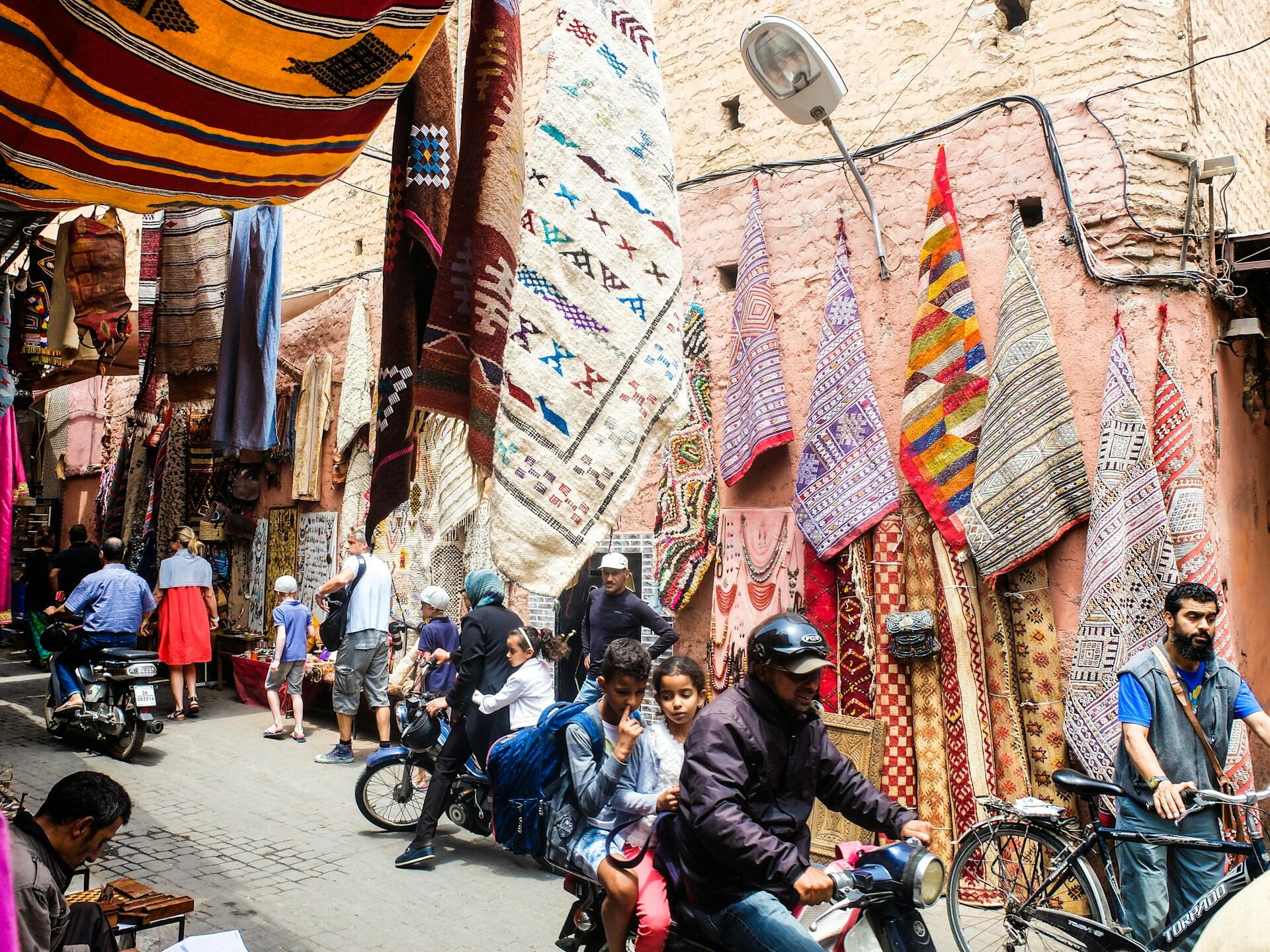 Straße mit Marktstand mit Teppichen und menschen auf Motorrädern.