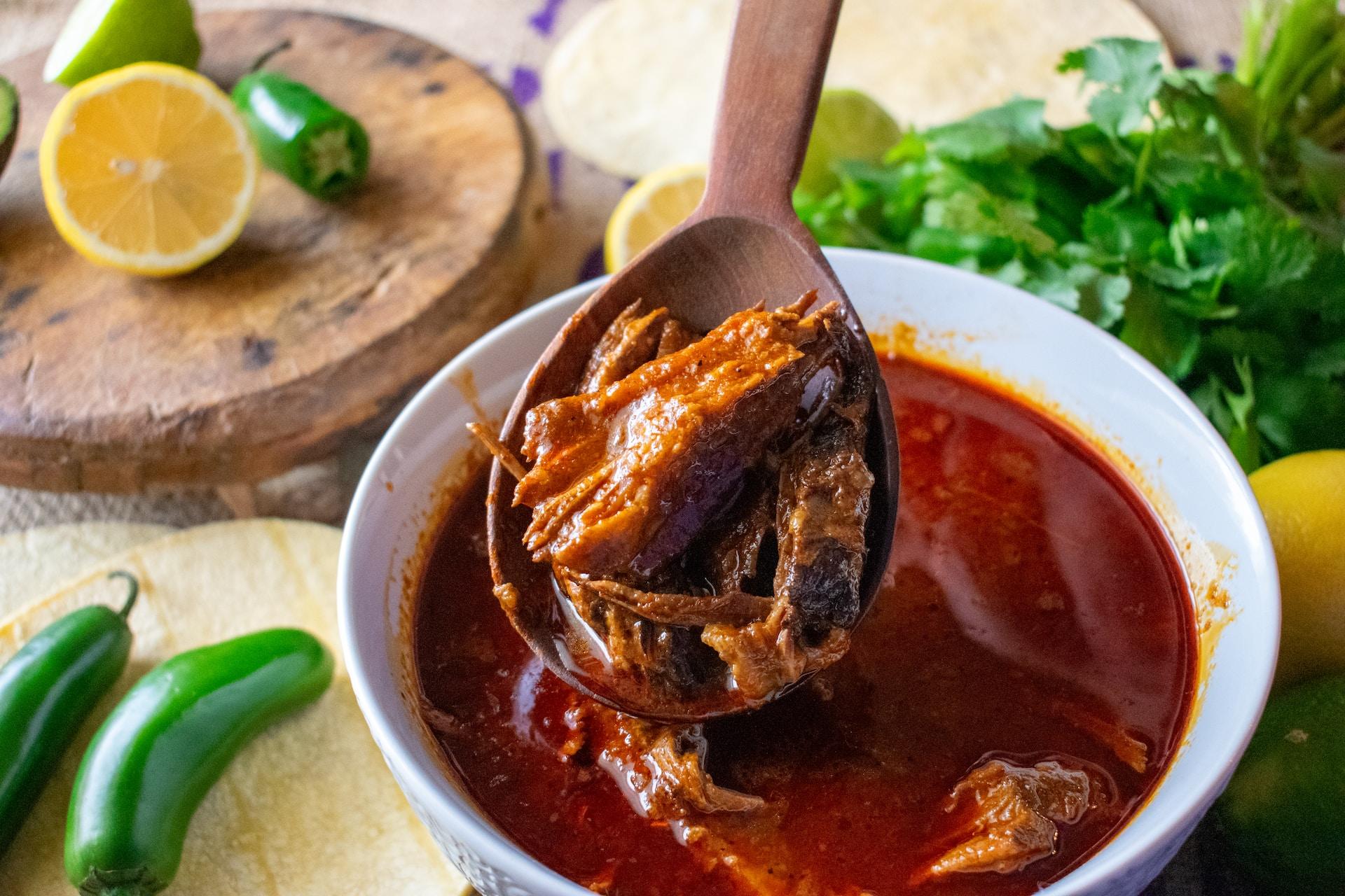Eintopfgericht mit Tomatensauce und Fleisch wird mit Holzlöffel aus weisser Schüssel geschöpft.