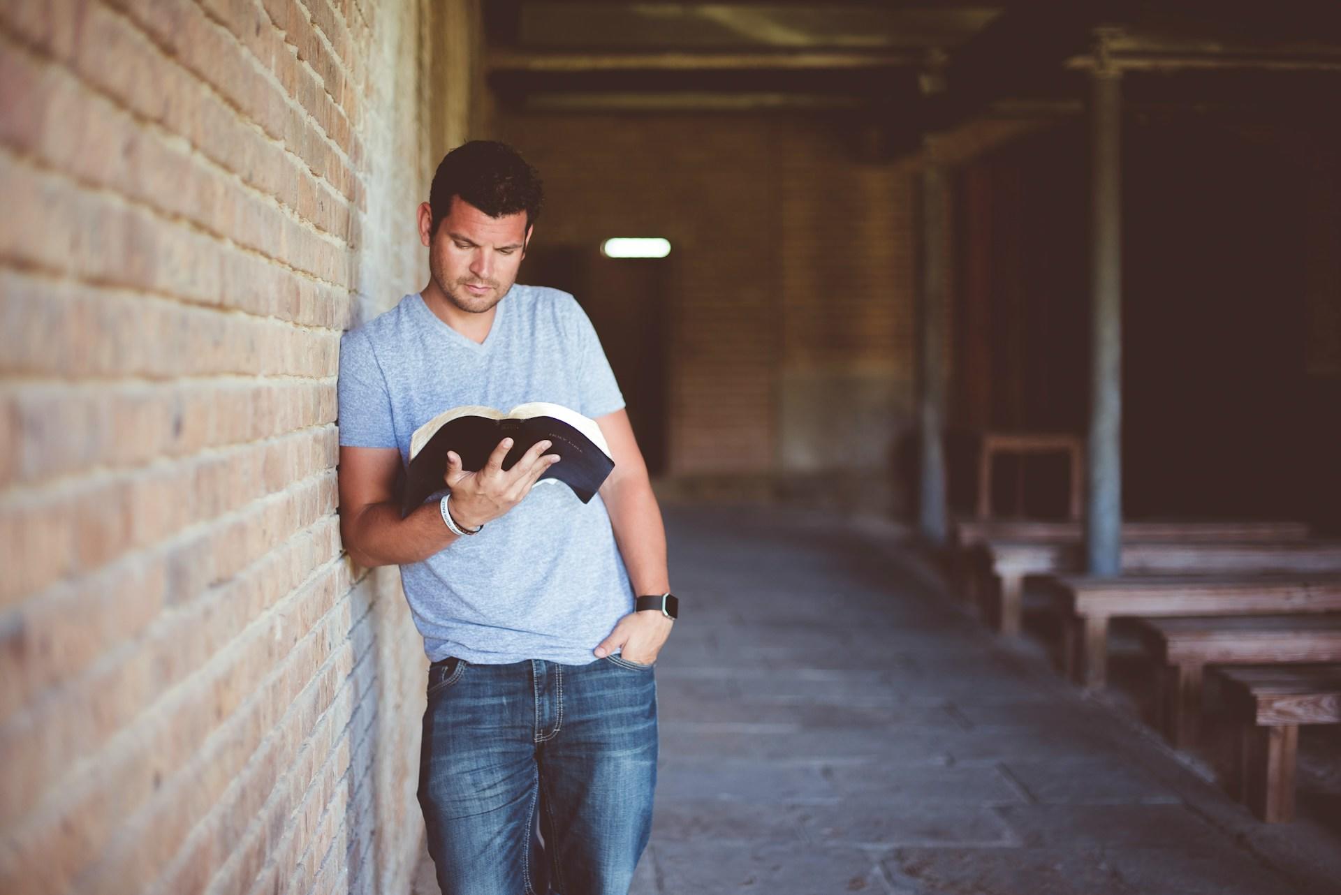 Eine Person steht an eine Mauer gelehnt und schaut in das offene Buch in ihrer Hand
