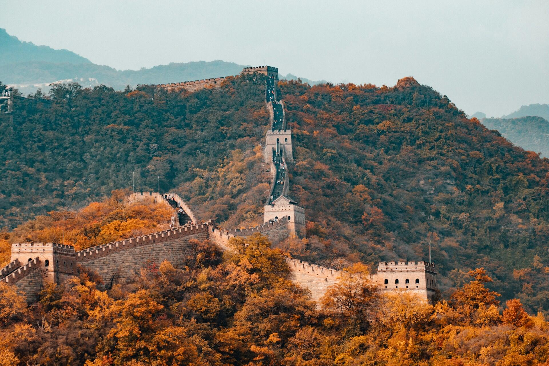 Mauer mit Türmen geht durch Berge mit Wald.