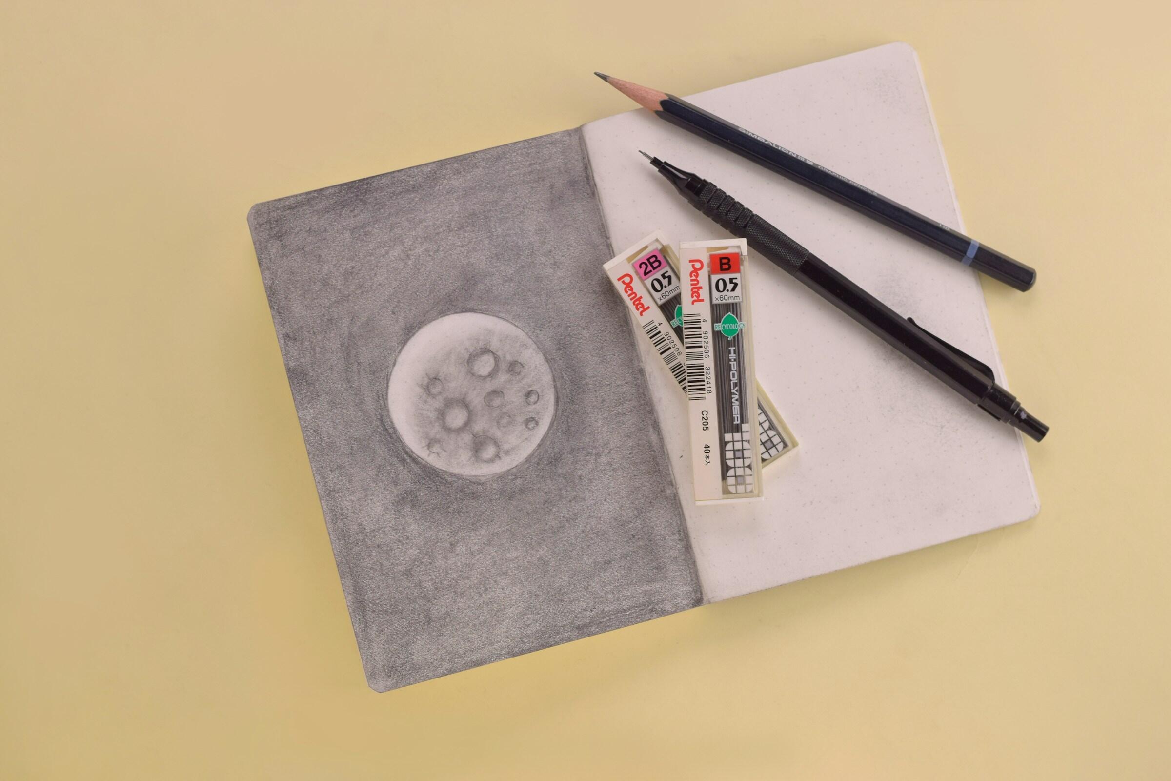 Ein Zeichenbuch mit einer Mond-Zeichnung und einem Druckbleistift.