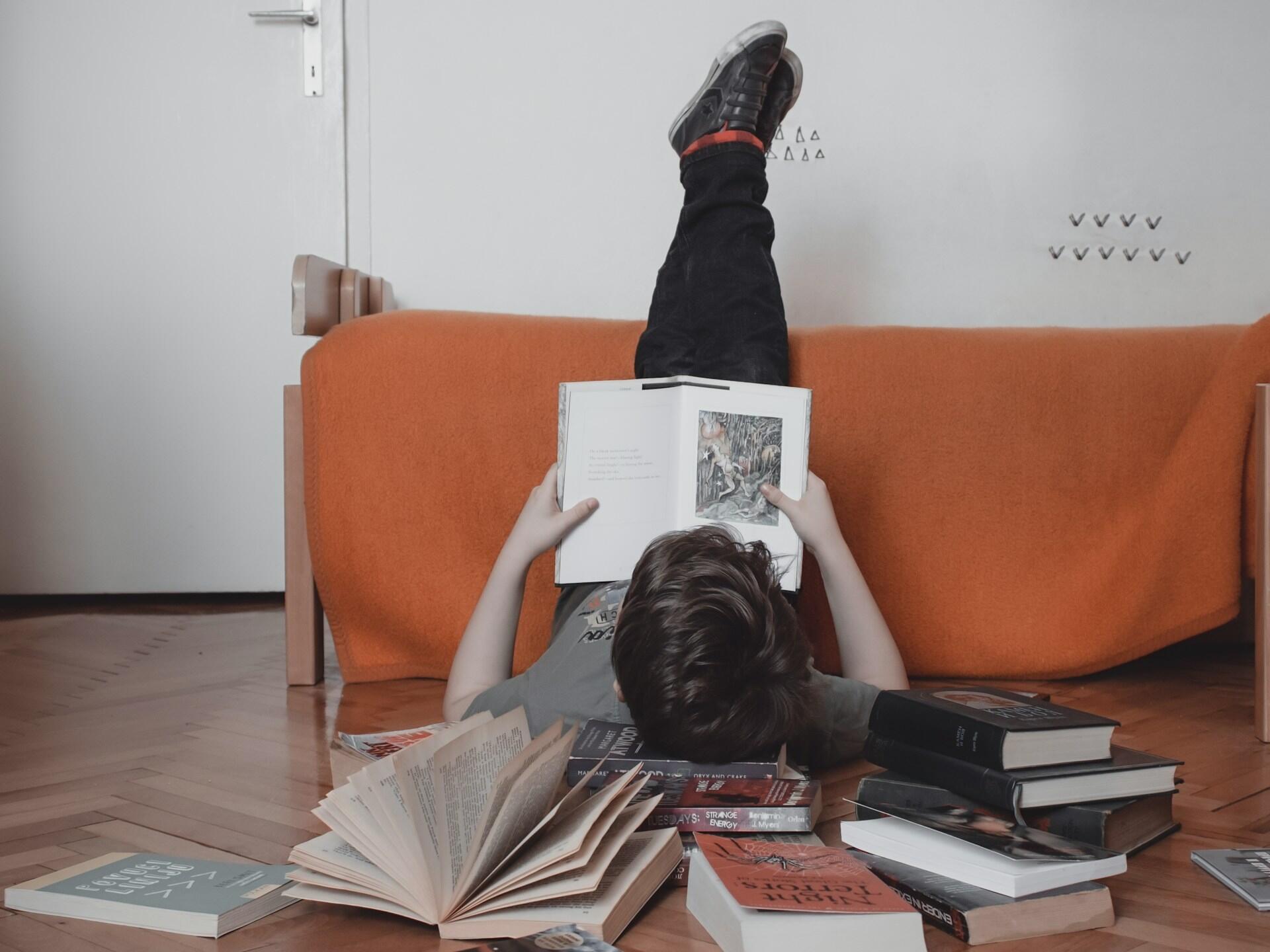 Ein Junge liegt lesend auf dem Boden, umringt von Büchern
