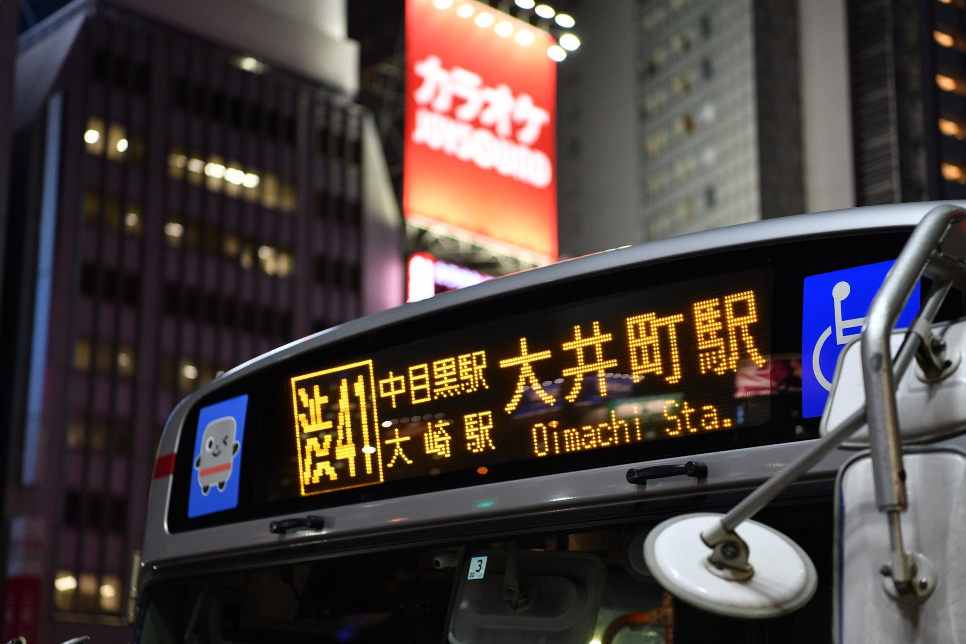 Bus mit japanischer Schrift vor hohen Gebäuden.