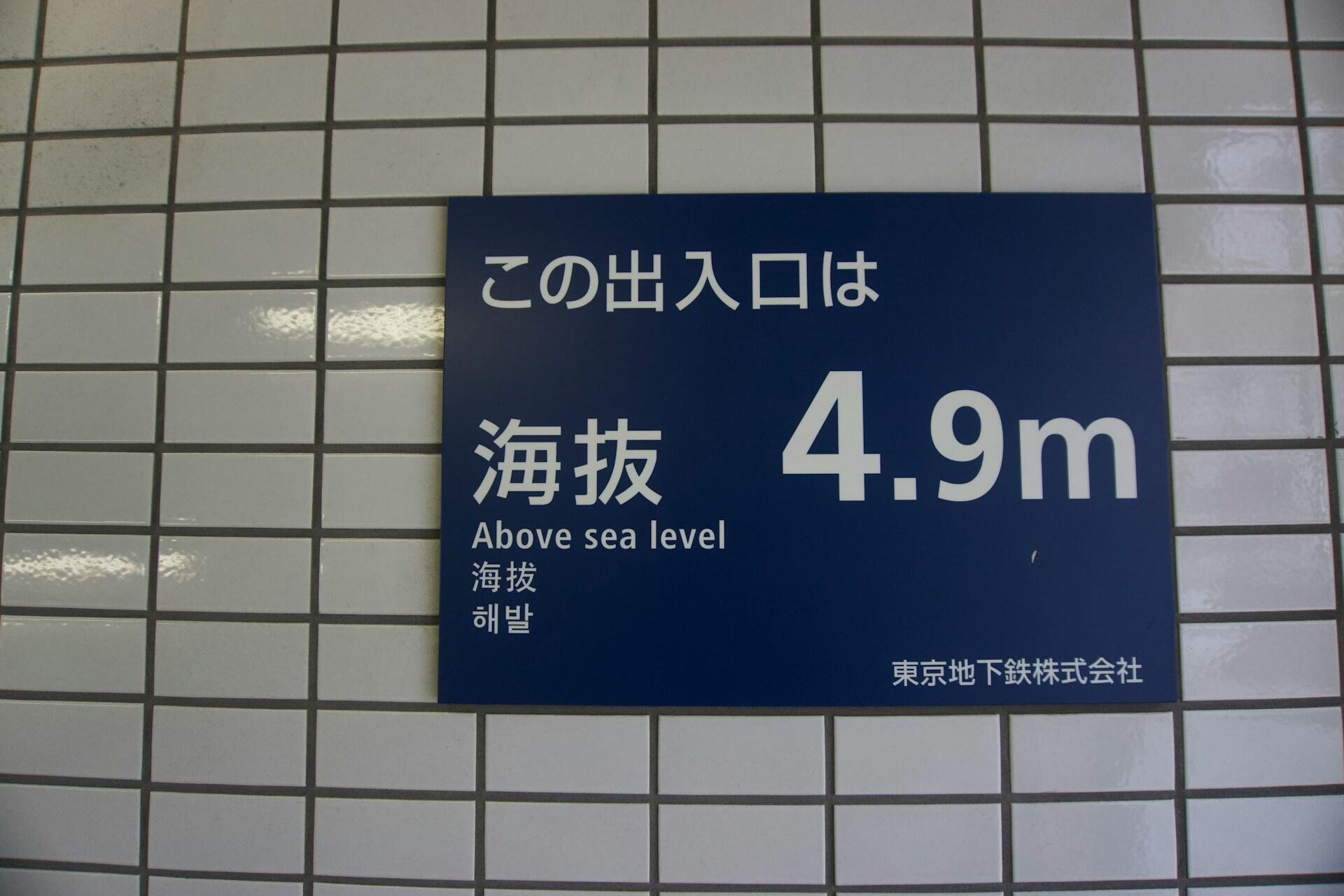 Blaues Schild mit weißer japanischer Schrift an gekachelter Wand.