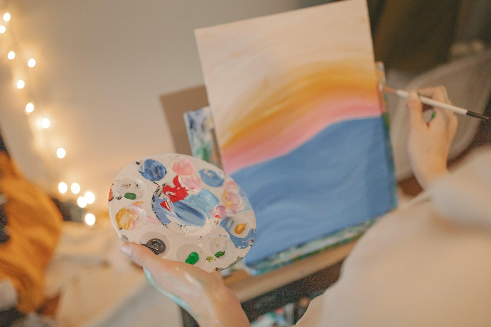 Eine Person hält eine Palette in der Hand und malt auf einer Leinwand