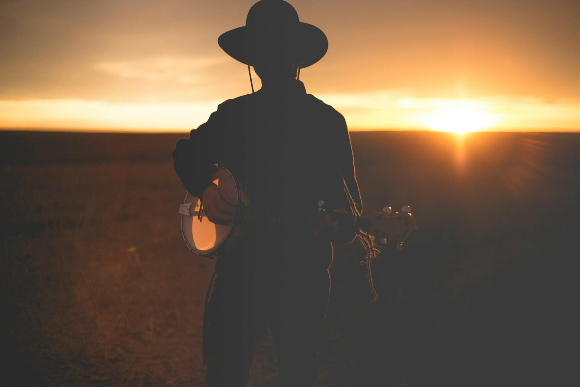 Mann mit Hut und Gitarre vor Sonnenuntergang.