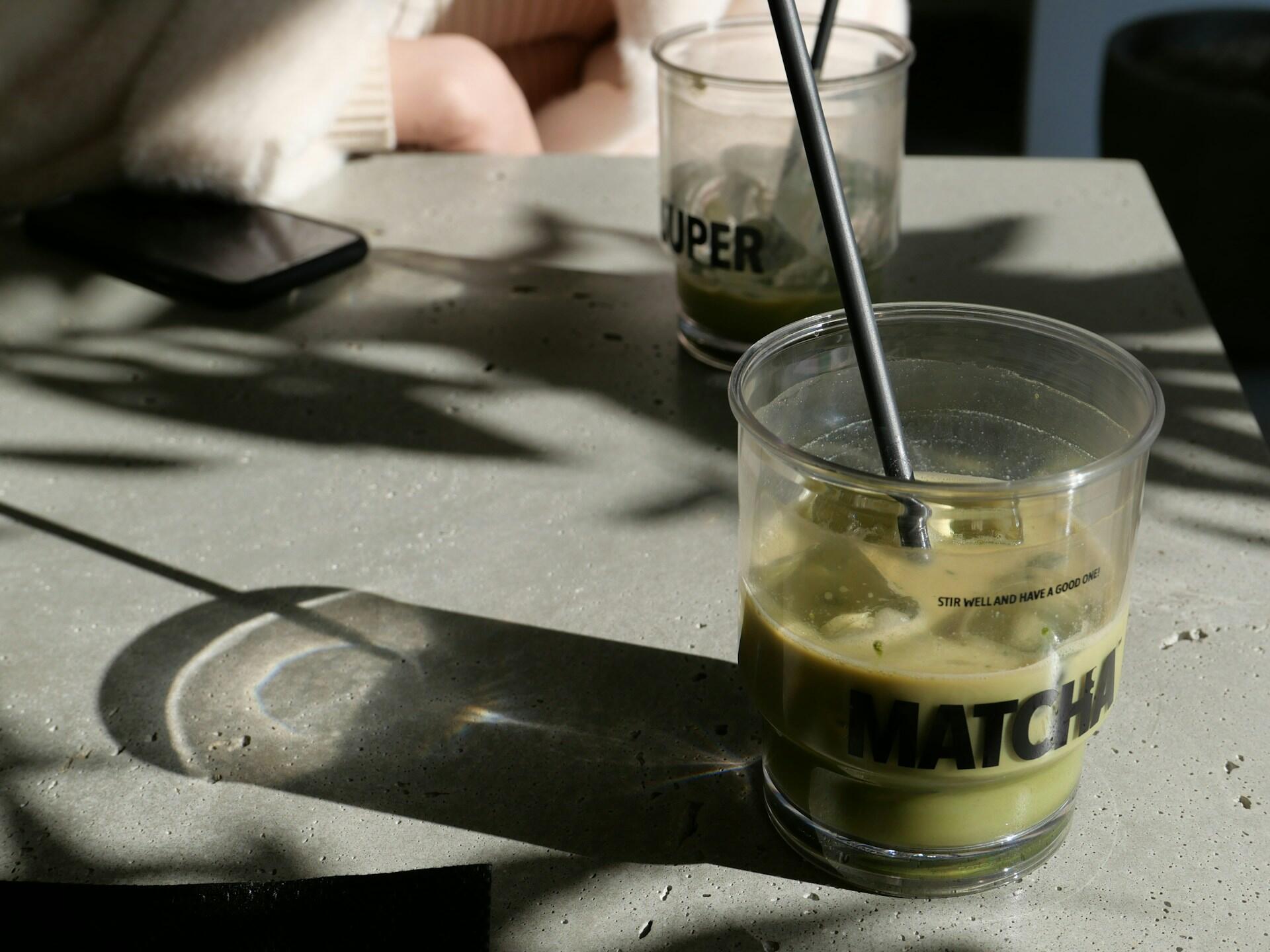 Zwei Gläser mit Strohhalm auf grauem Steintisch.