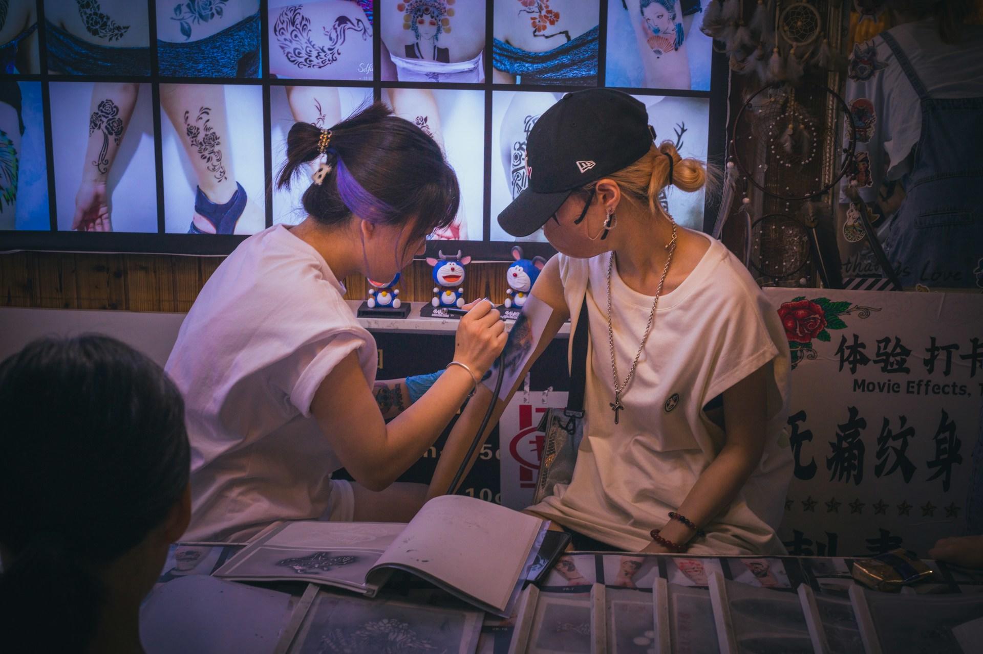 Eine Frau tätowiert eine andere Frau in einem dunklen Raum.