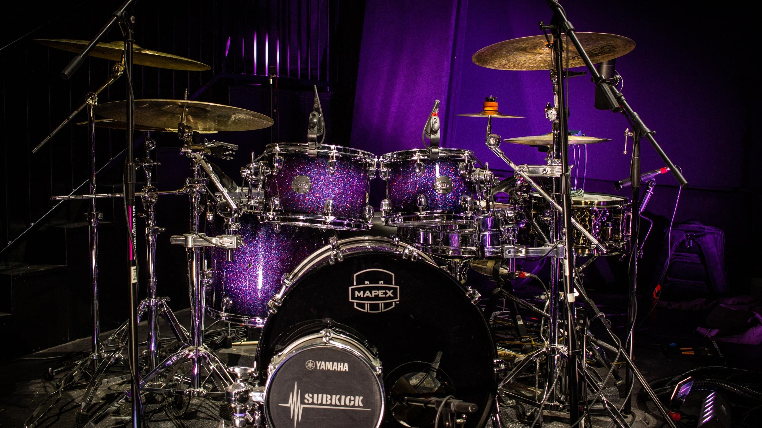 Ein komplettes Drumset ist vor lilanem Hintergrund aufgebaut.