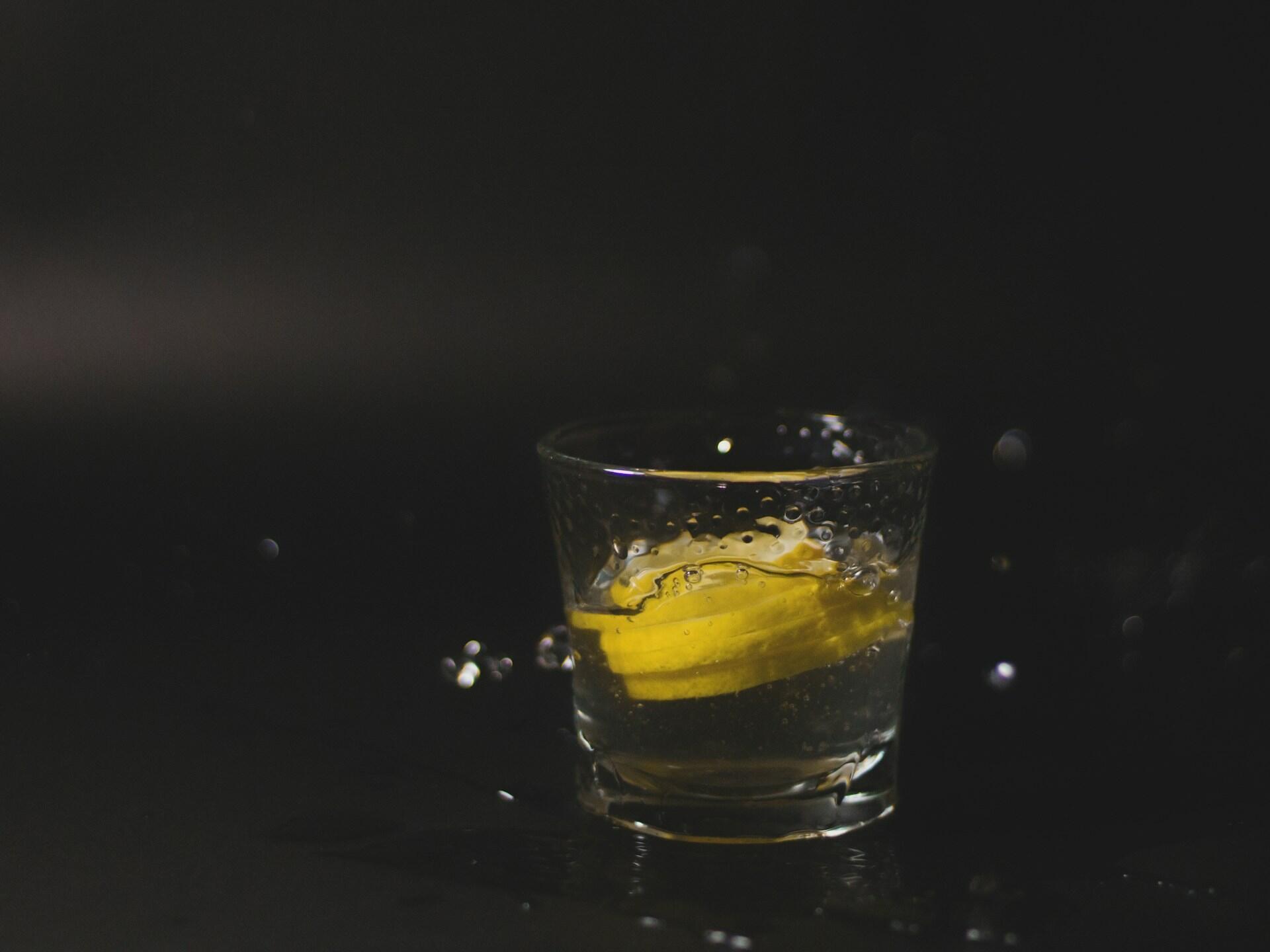 Glas mit Wasser und Zitrone vor dunklem Hintergrund.