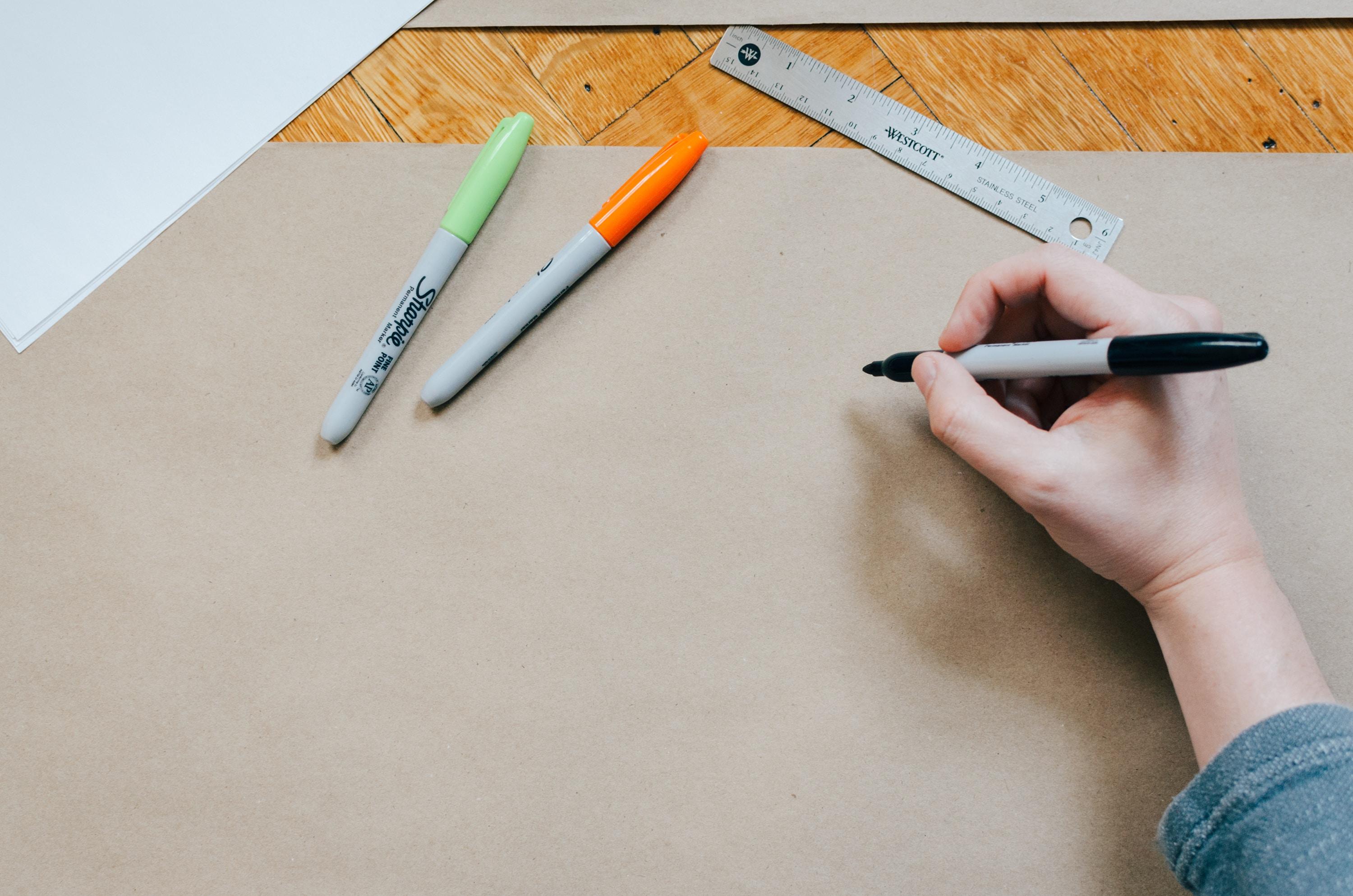 Hand hält Stift und zeichnet auf braunem Papier.