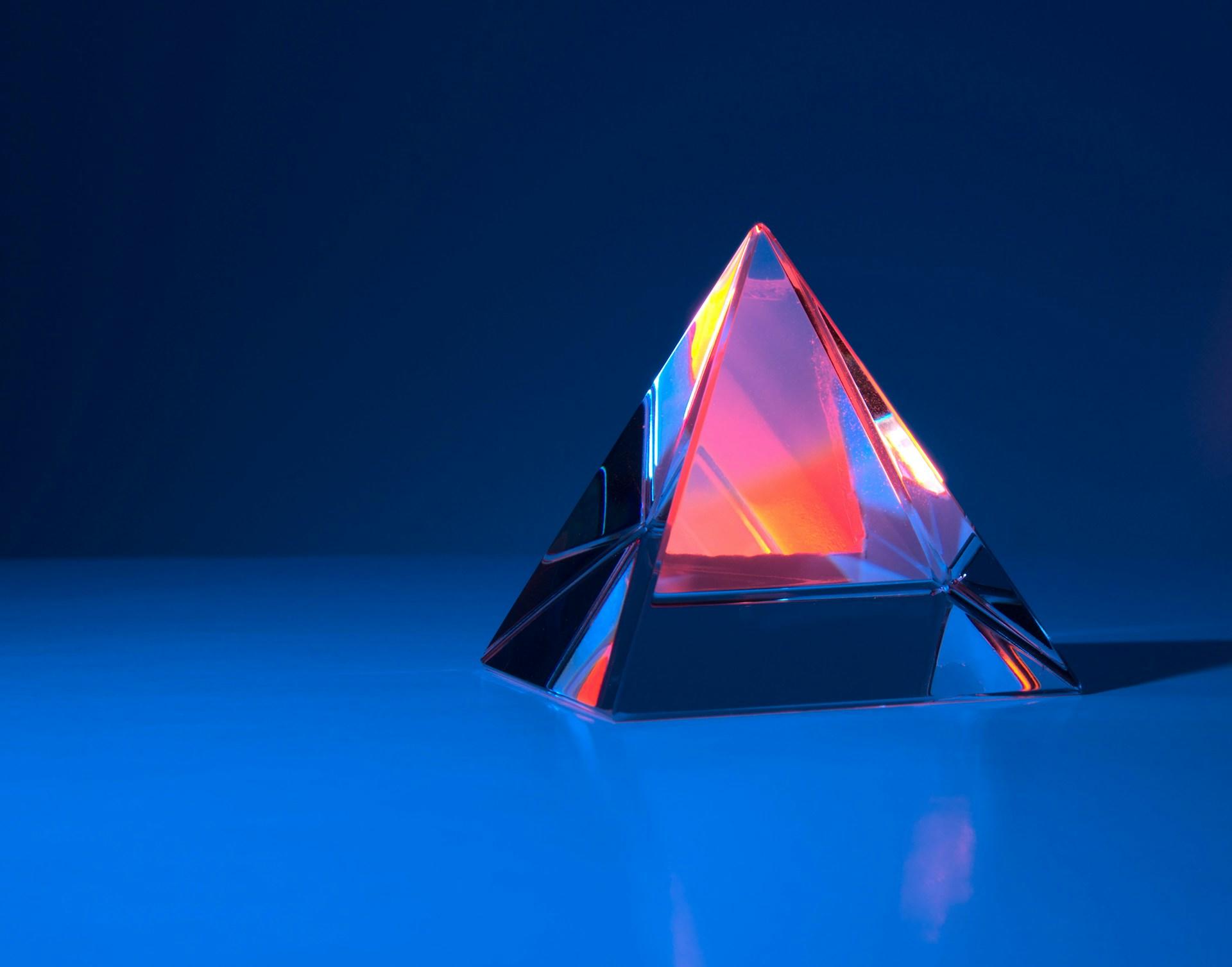In einer Pyramide aus Glas auf blauem Untergrund bricht sich das Licht.