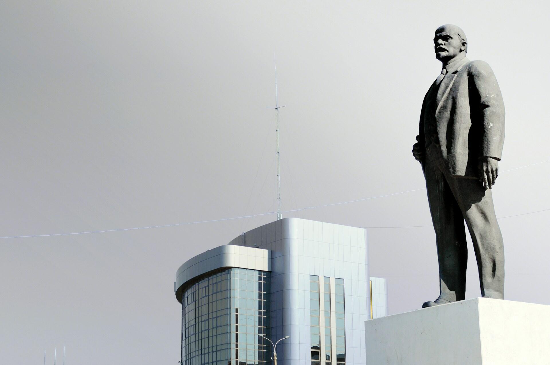 Graue Betonstatue von Mann auf Sockel.