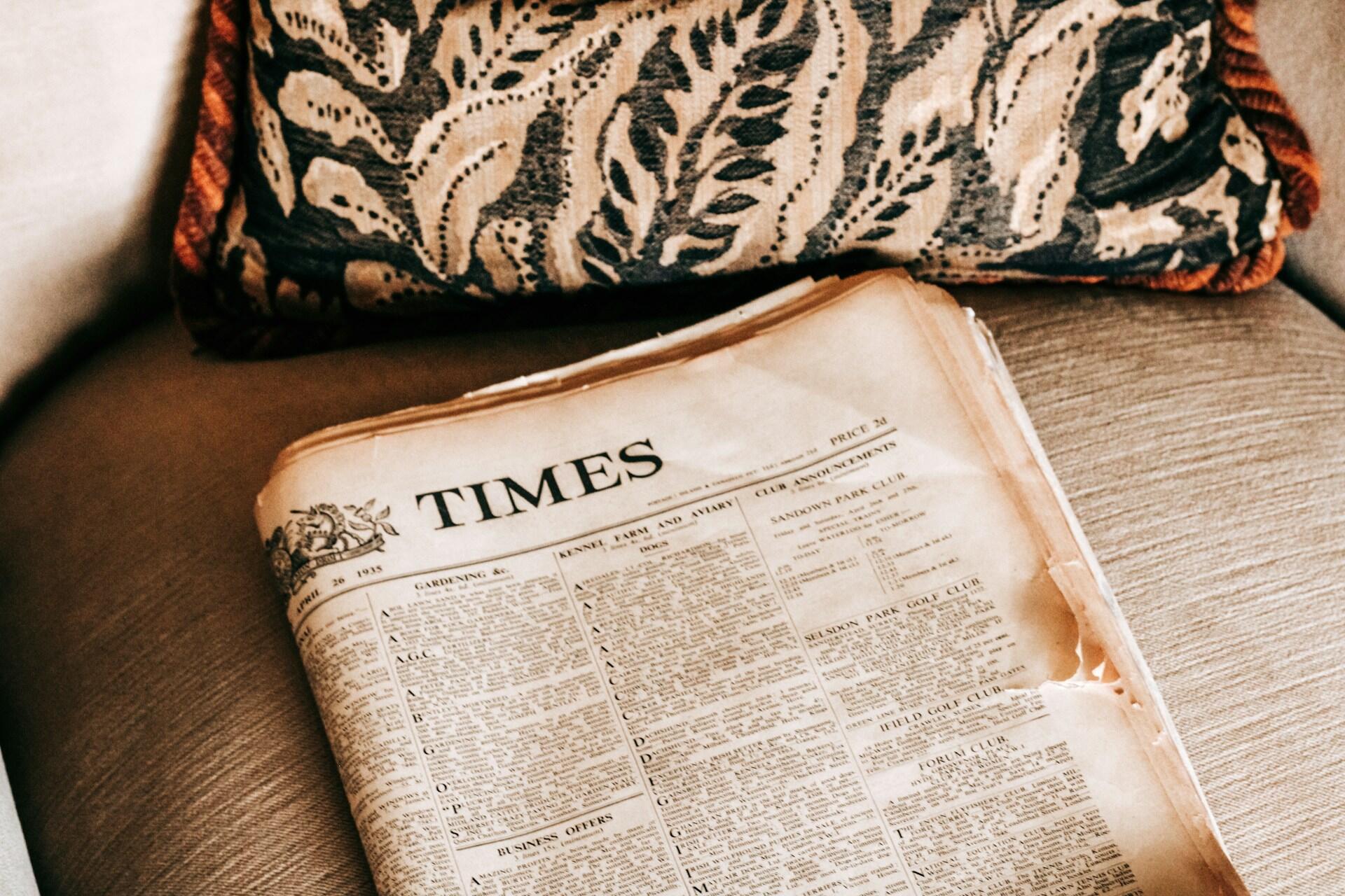 Zeitung liegt auf Sofa neben Kissen.