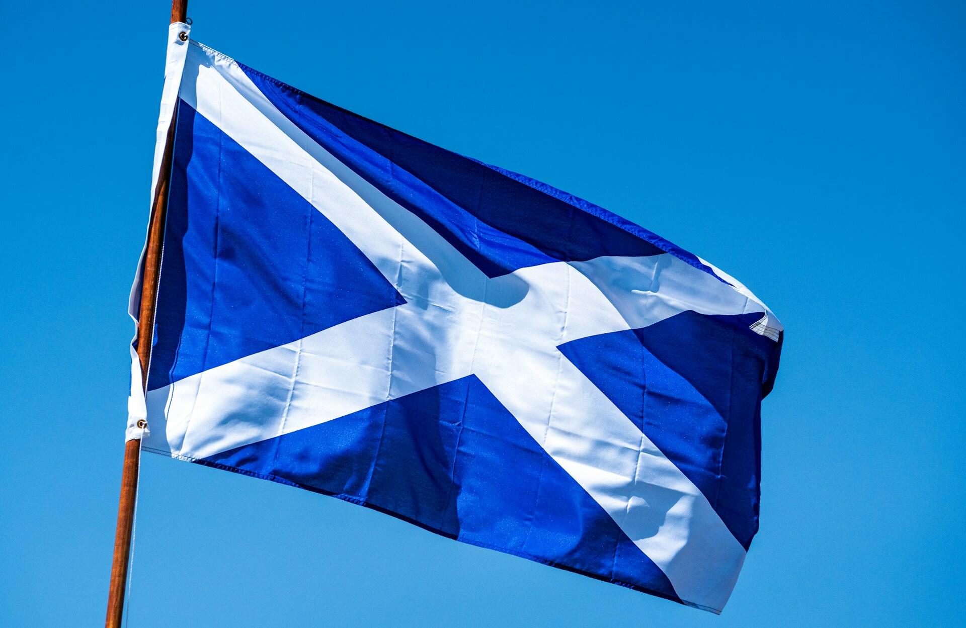 Blaue Flagge mit weißem Diagonalkreuz an Mast.