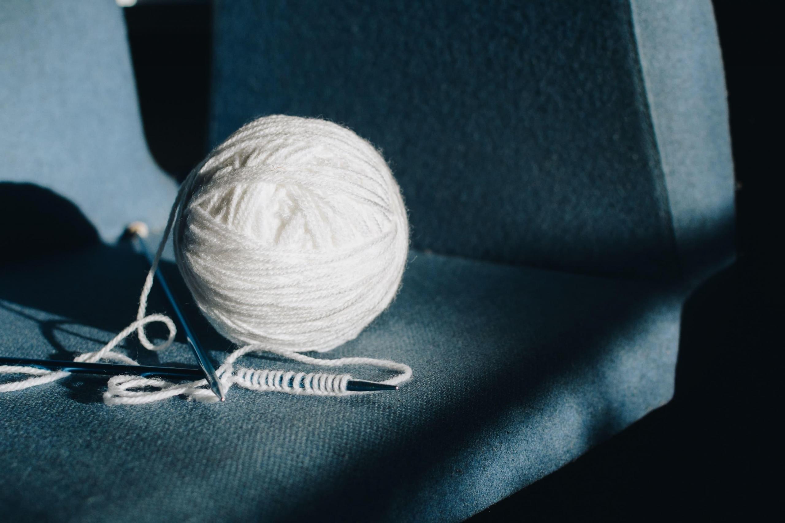 Ein weißes Wollknäuel und eine Stricknadel