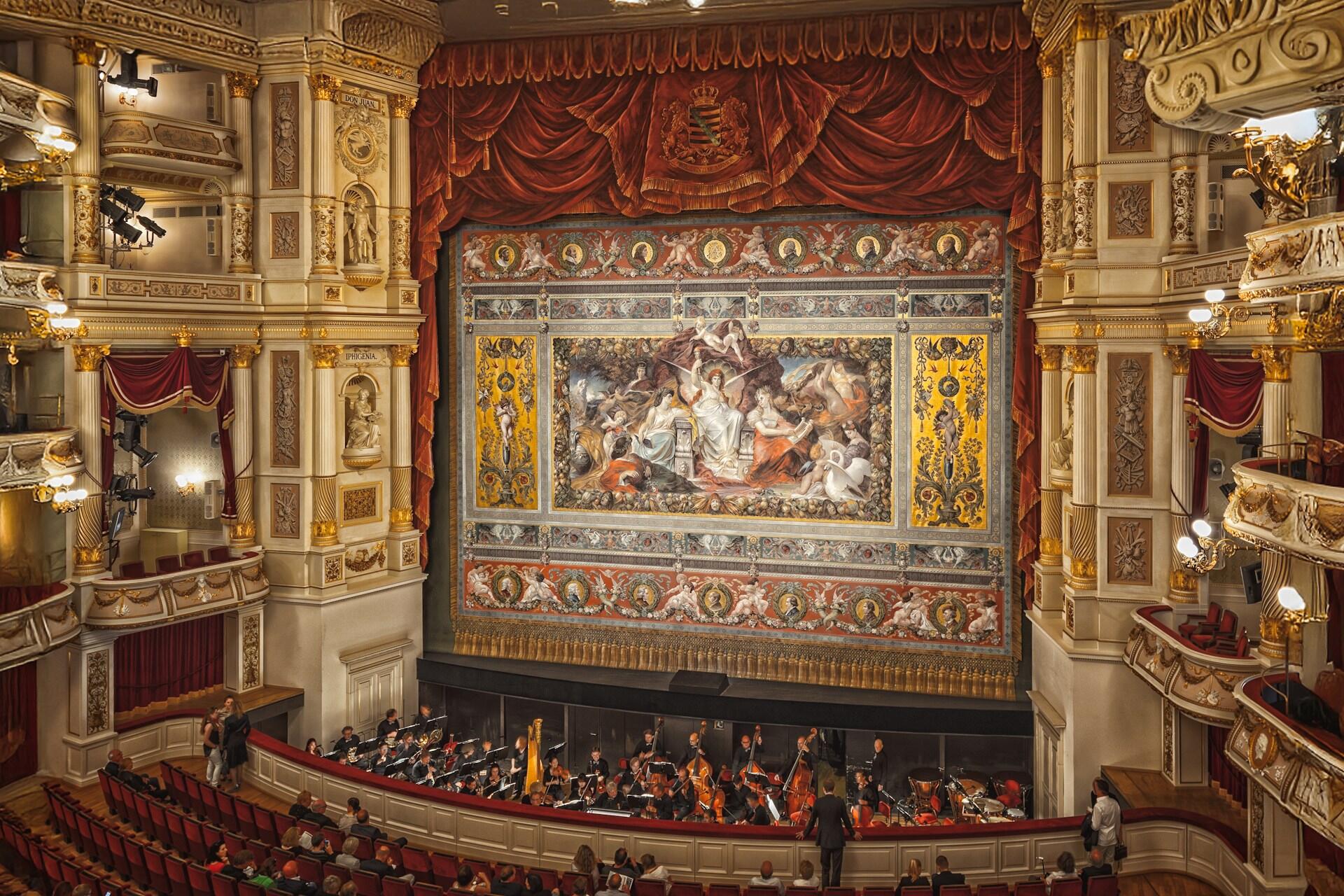 Oper mit Orchester vor bunter Bühne.