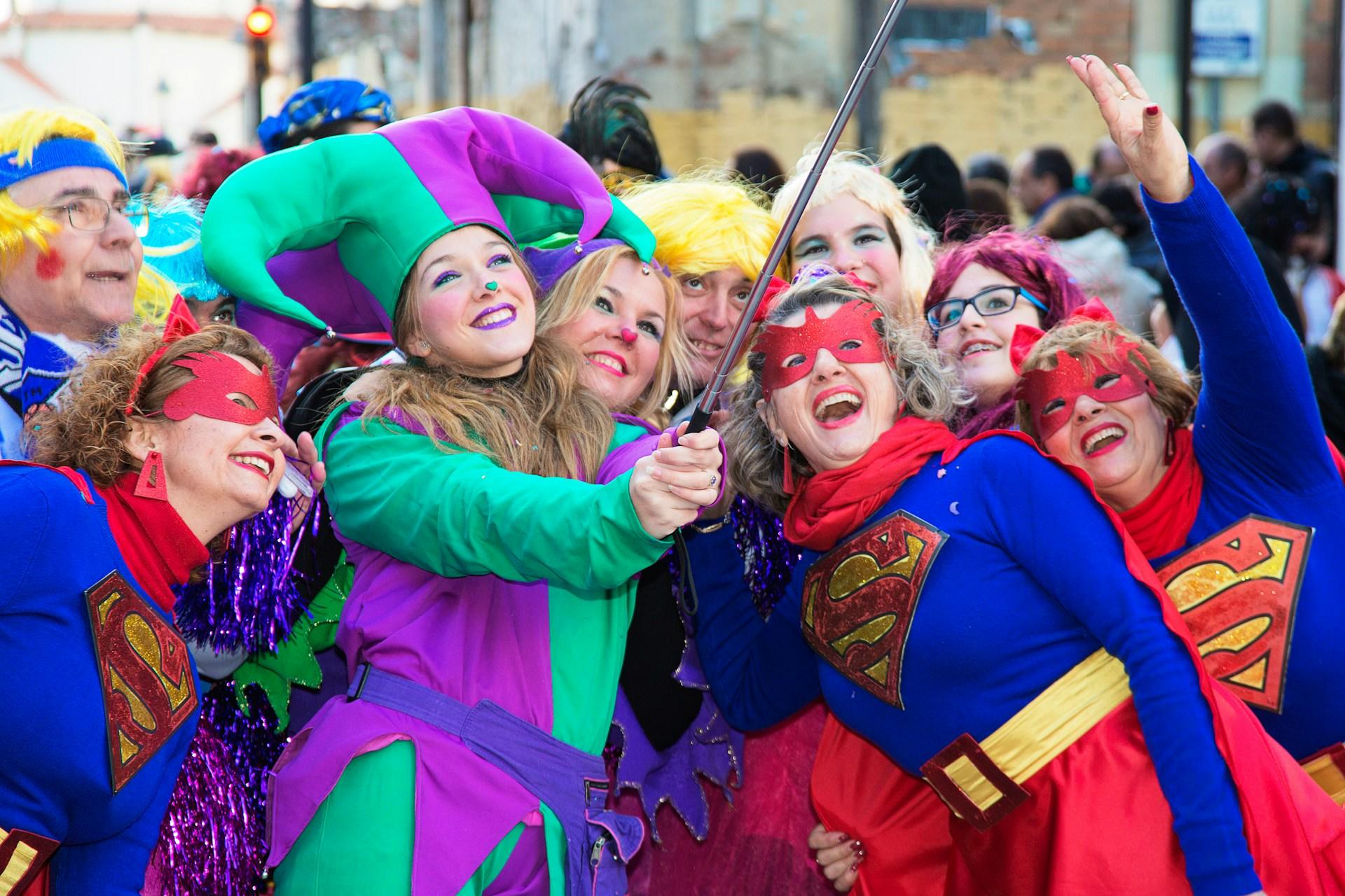 Frauen in bunten Faschingskostümen posieren auf einem Platz in Deutschland und eine Frau macht ein Foto mit dem Selfiestick.