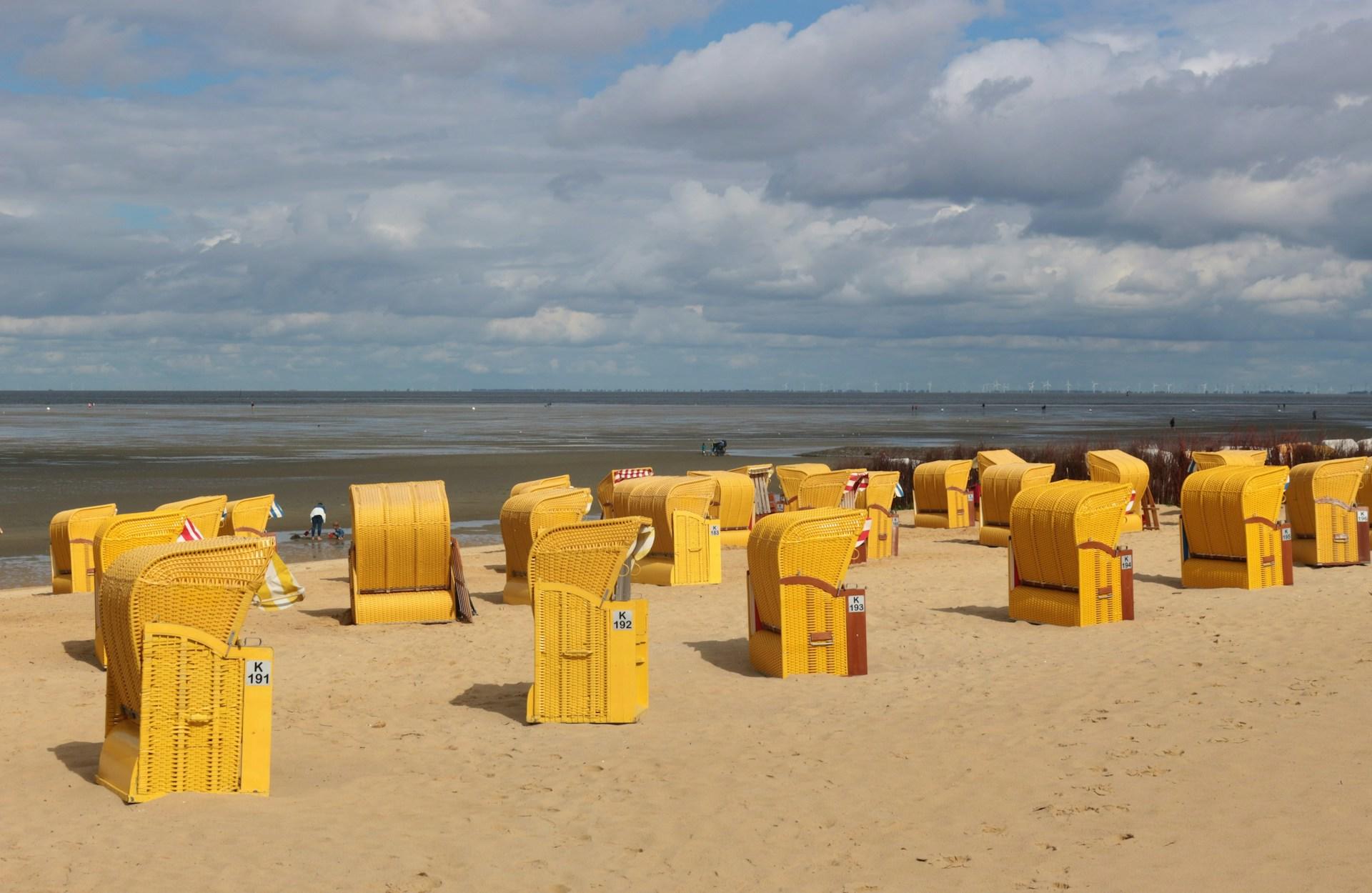 Typisch Deutsch sind auch die gelben Strandstühle in Cuxhafen vor grauem Himmel und dem Meer.
