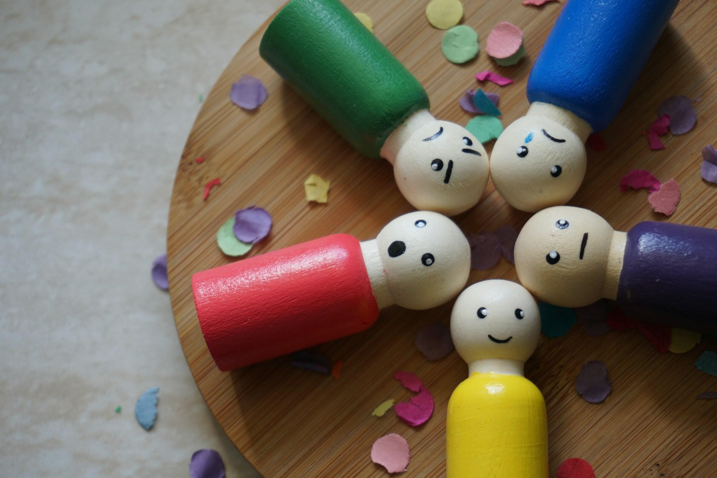 Mehrere bunte Holzfiguren mit verschiedenen Gesichtern, die Emotionen repräsentieren.