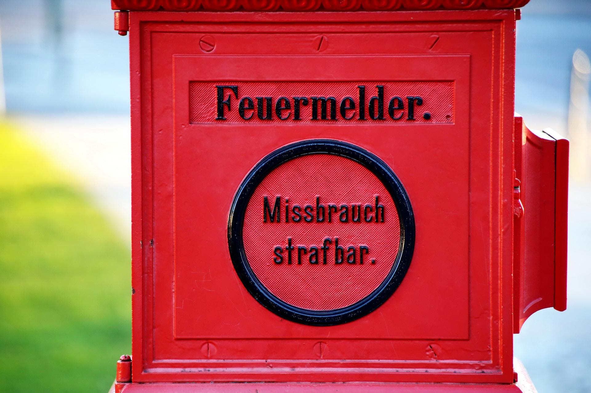 Eine rote Eisenvorrichtung mit schwarzer Aufschrift Feuermelder Missbrauch strafbar sorgt im Straßenbild für Aufmerksamkeit.