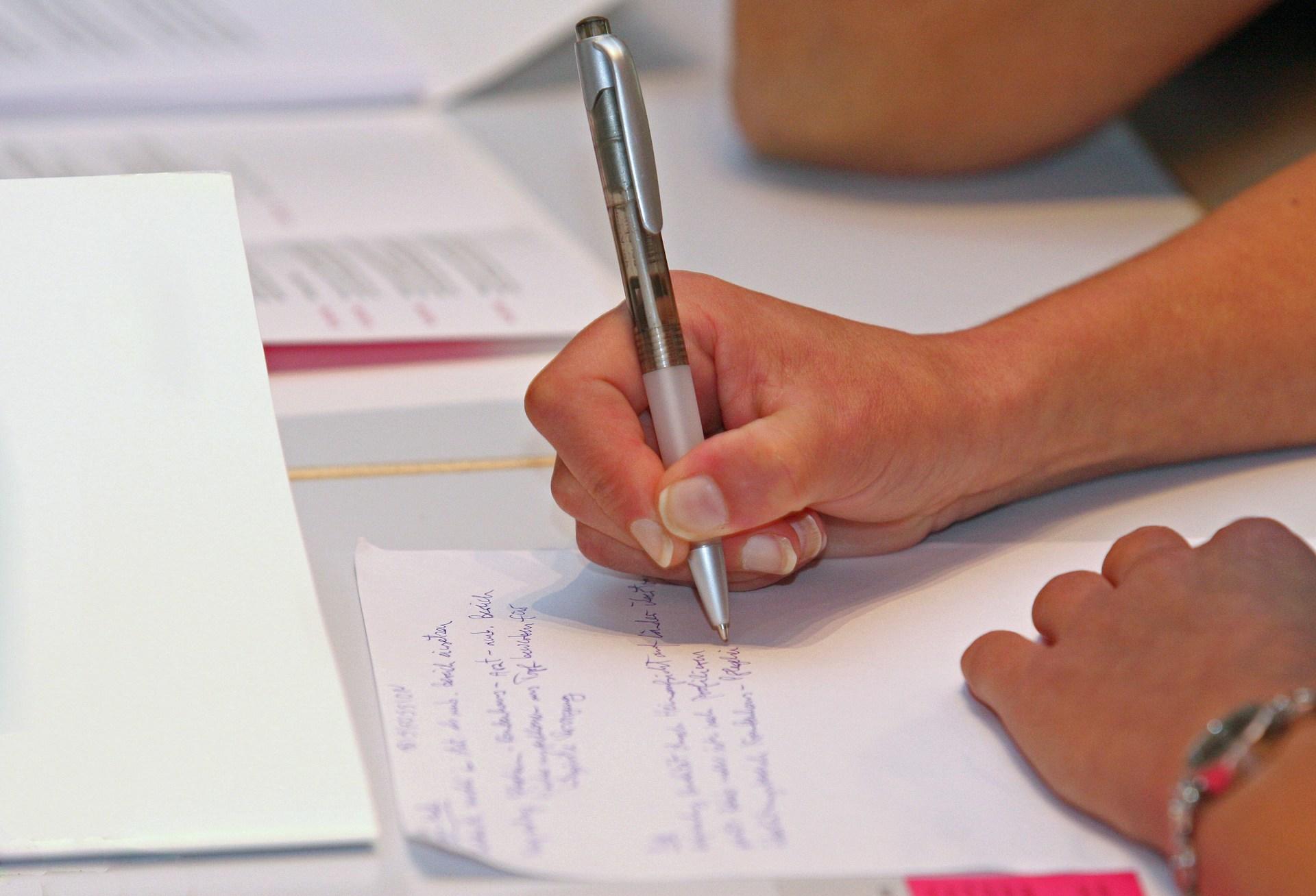 Person mit Stift schreibt auf Zettel.