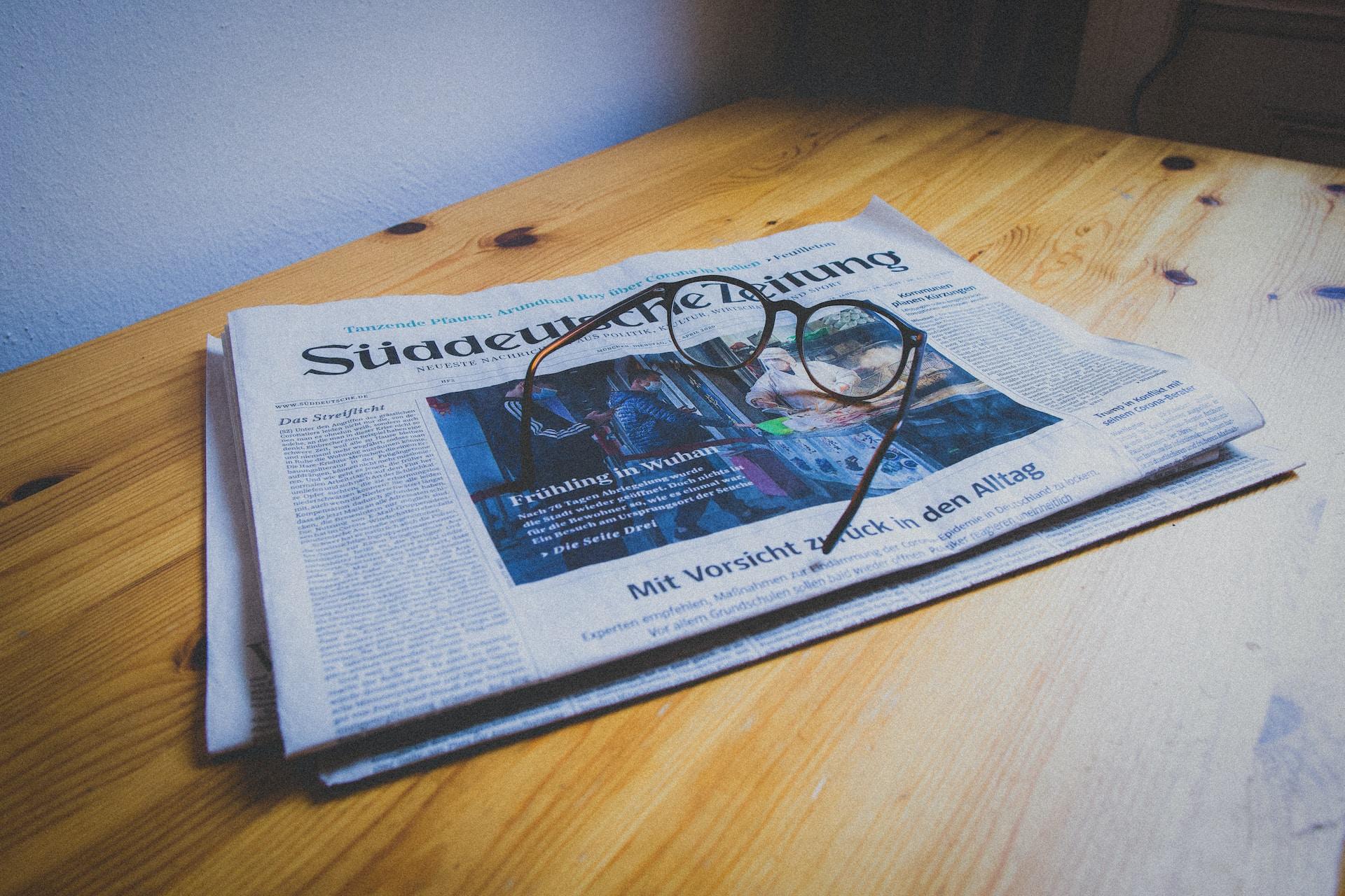 Auf einem Holztisch eine Süddeutsche Zeitung die in der neuen Rechtschreibung verfasst ist und darauf liegt eine Brille.