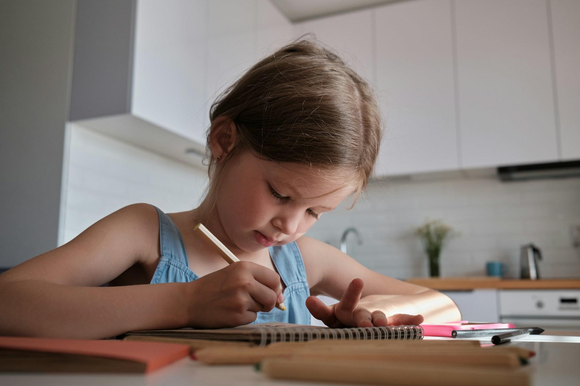 Kleines Mädchen sitzt mit Stift und Notizheft an einem Tisch
