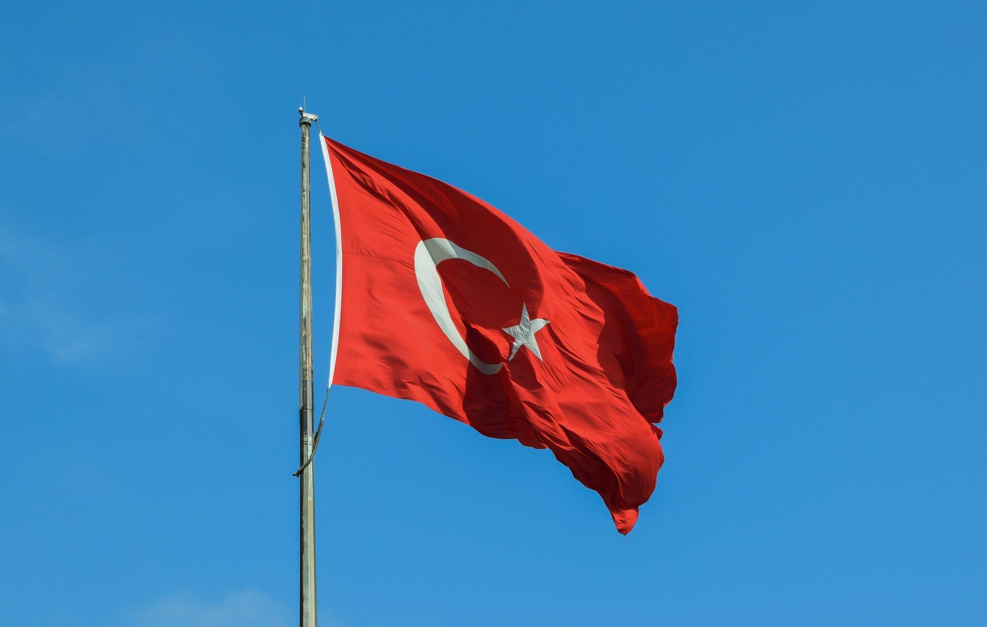 Rote Flagge mit weißem Halbmond an Mast vor blauem Himmel.