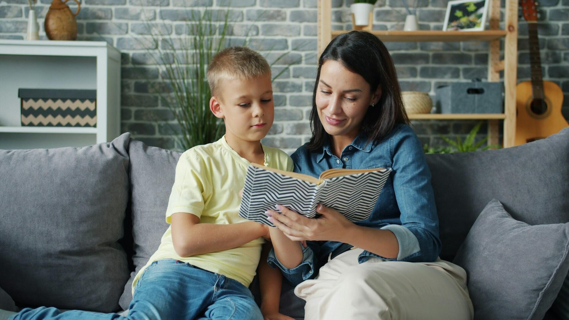 Frau und Junge sitzen auf Sofa und lesen ein Buch.