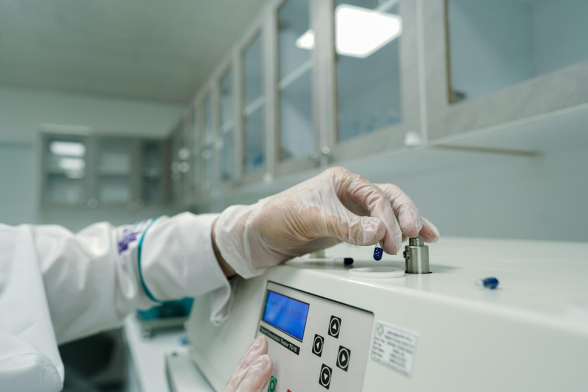 Person mit Kittel und Handschuhen bedient Gerät im Labor.