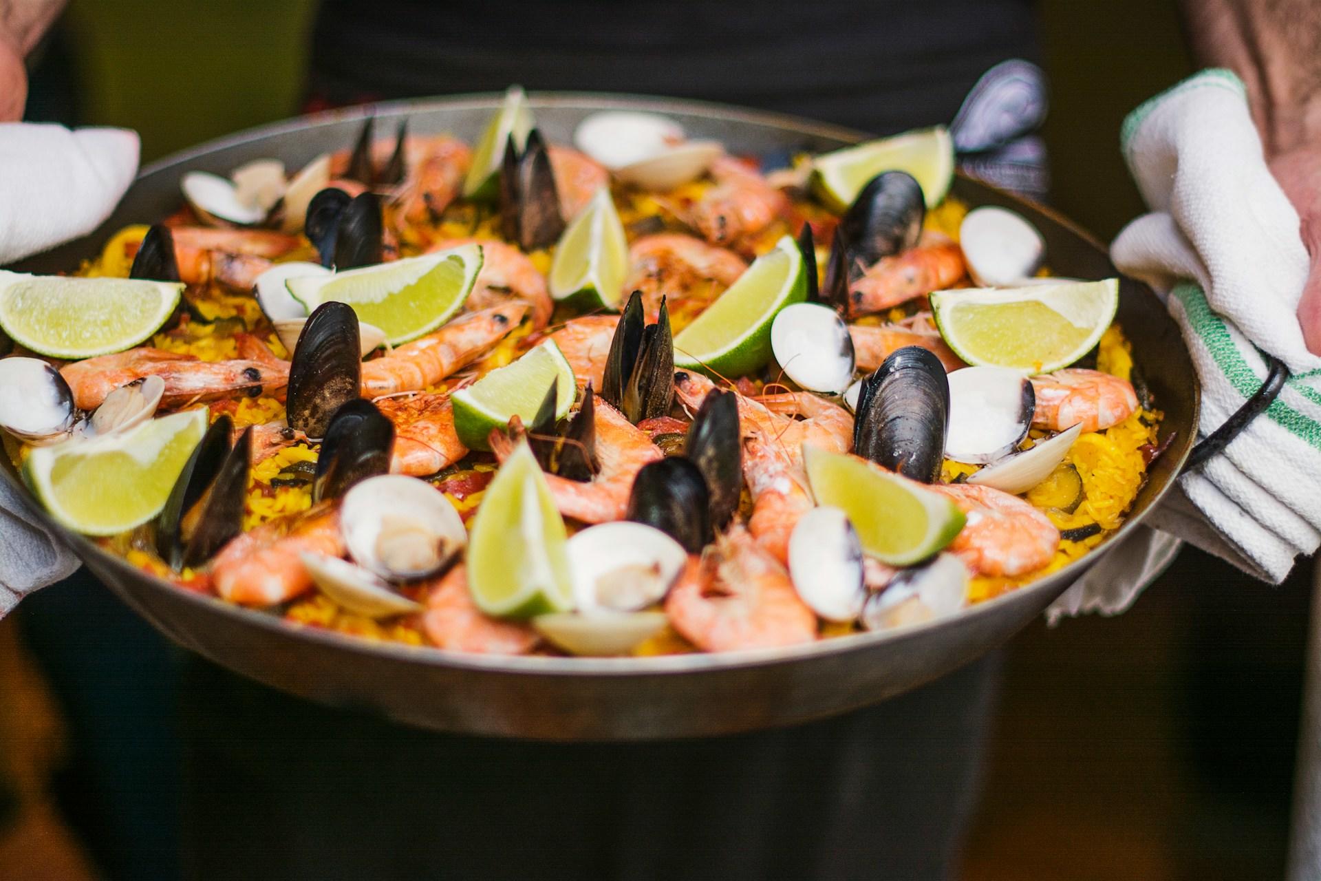 Eine typische Pfanne mit spanischer Paella wird von beiden Seiten mit Küchenlappen gehalten.