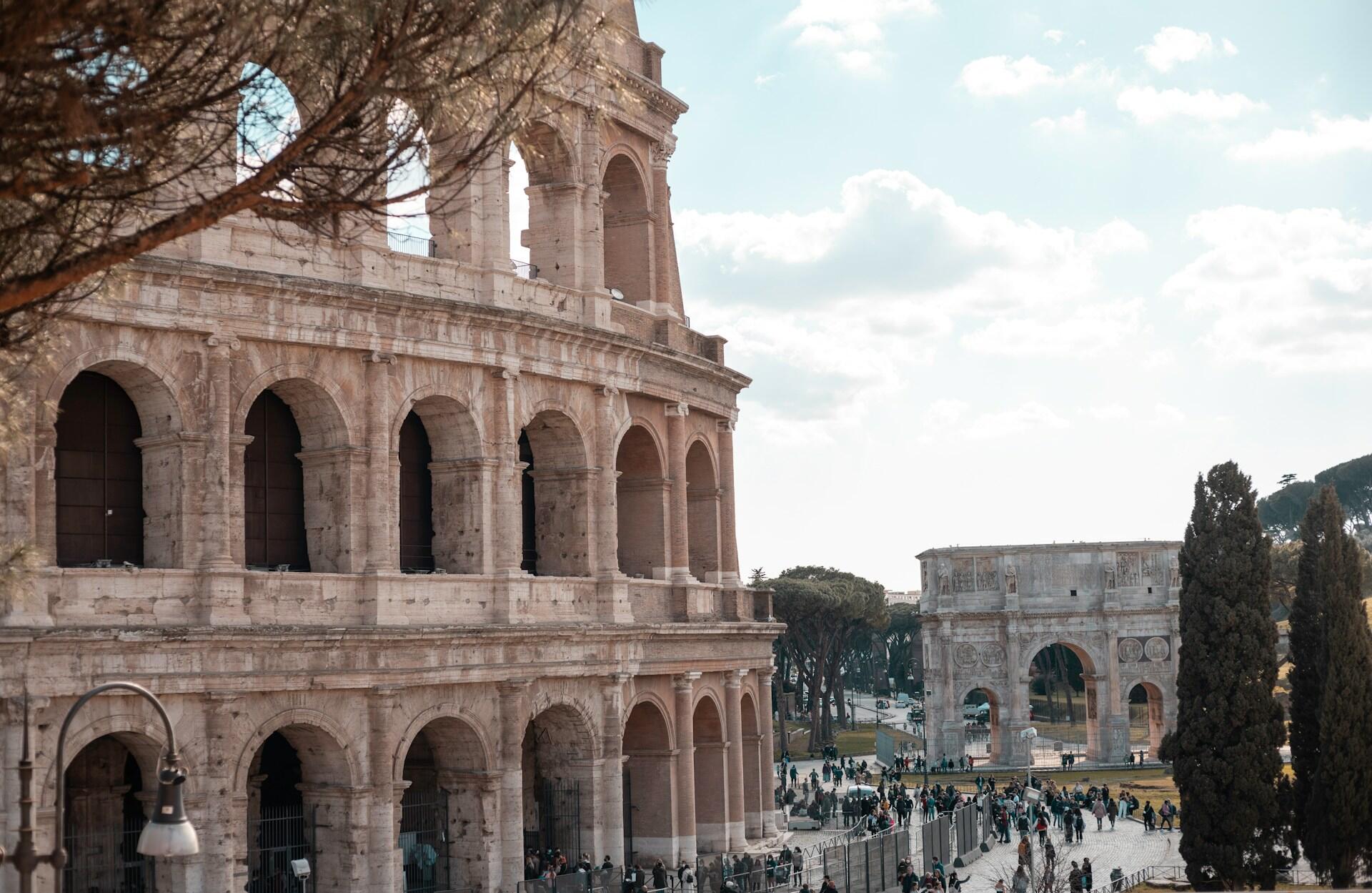 Steingeböude mit Fenster vor Triumphbogen und Bäumen.