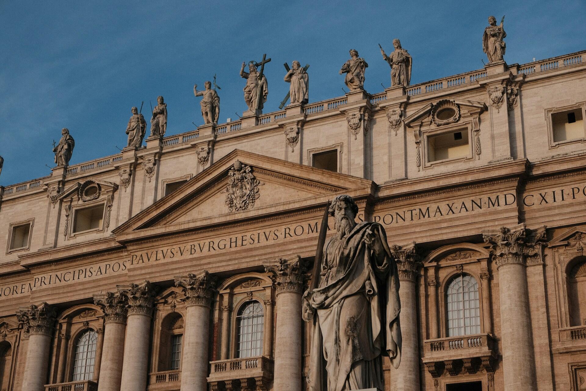 Gebäude mit lateinischer Schrift und Statuen auf dem Dach.